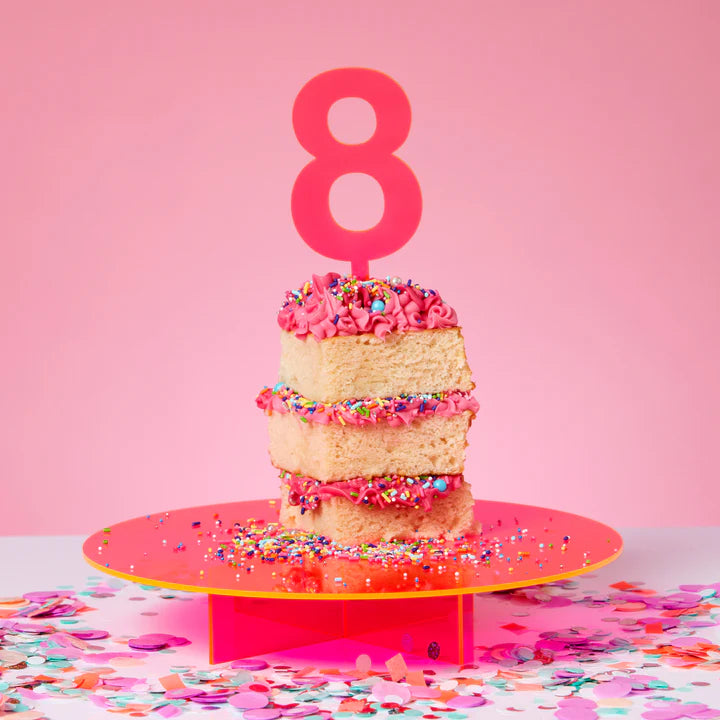 Number 8 large cake topper in neon pink in a cake on a pink cake stand.