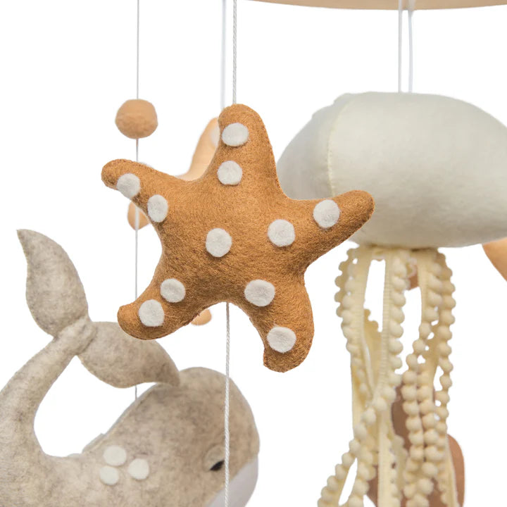 The ROOMI & ME Roomi & Me - Baby Mobile Underwater Dreaming features handmade felt sea creatures like a brown starfish, whale, and jellyfish with textured tentacles, designed for gentle visual stimulation in any nursery.