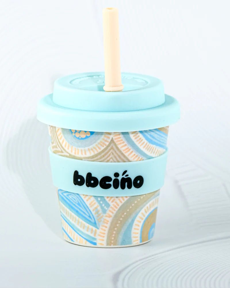 The BBcino - Reusable Babycino Cup 120ml Coast by BBCINO features a pastel blue lid and straw, a geometric blue, beige, and white pattern, and an eco-friendly design with a matching sleeve printed with the brand name.
