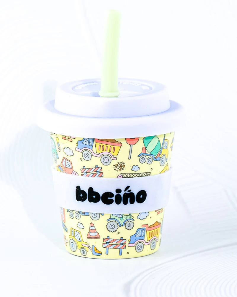 The BBcino ~ Reusable Babycino Cup 120ml Dig It features a colorful, toddler-sized design with cartoon construction vehicles and animals on yellow. It includes a green straw and lid, eco-friendly materials, and the BBCINO brand name on a white band encircling it.