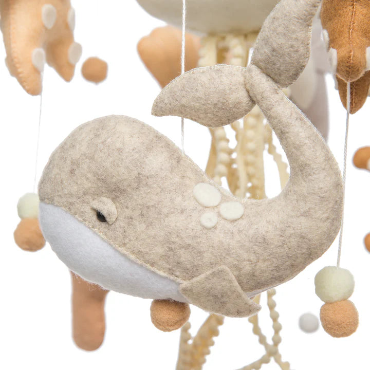 A close-up of ROOMI & ME's Roomi & Me - Baby Mobile Underwater Dreaming shows a soft beige and white felt whale, hanging among other sea creatures and neutral-toned beads—a handmade nursery décor for gentle visual stimulation.