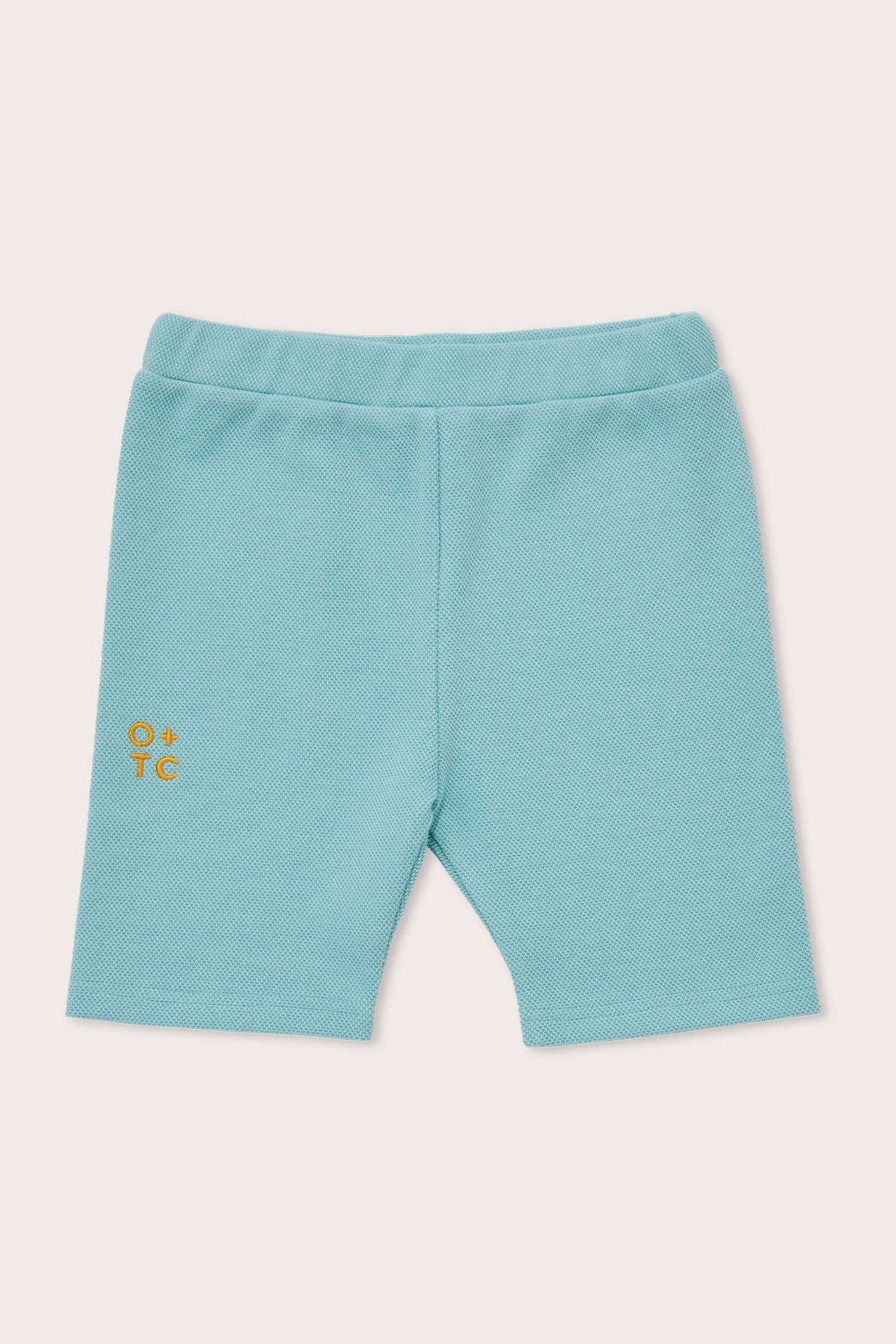 A pair of Aqua Sky toddler bike shorts with an elastic waistband. These premium fabric shorts feature a small, yellow-orange OLIVE + THE CAPTAIN logo on the left thigh. The background is a solid off-white color.