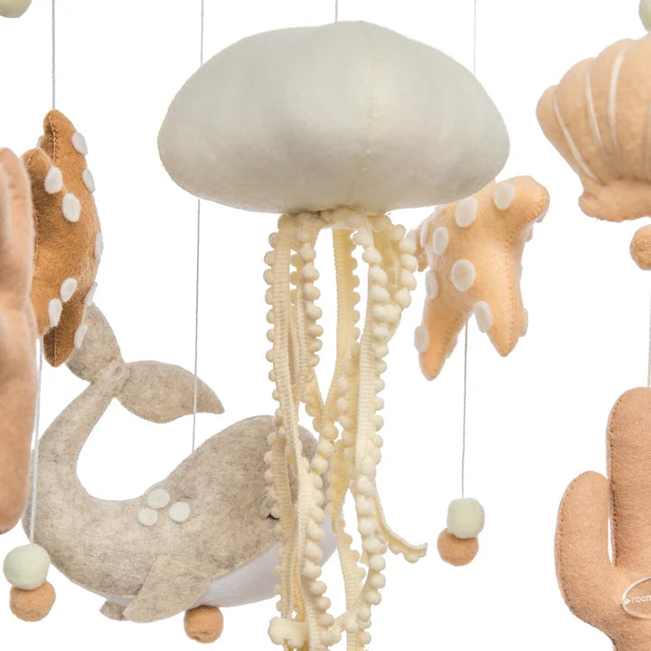 The ROOMI & ME "Roomi & Me - Baby Mobile Underwater Dreaming" is a soft, handmade mobile with felt sea creatures in neutral tones—gray whale, white jellyfish, starfish—perfect for nursery decor and visual stimulation.