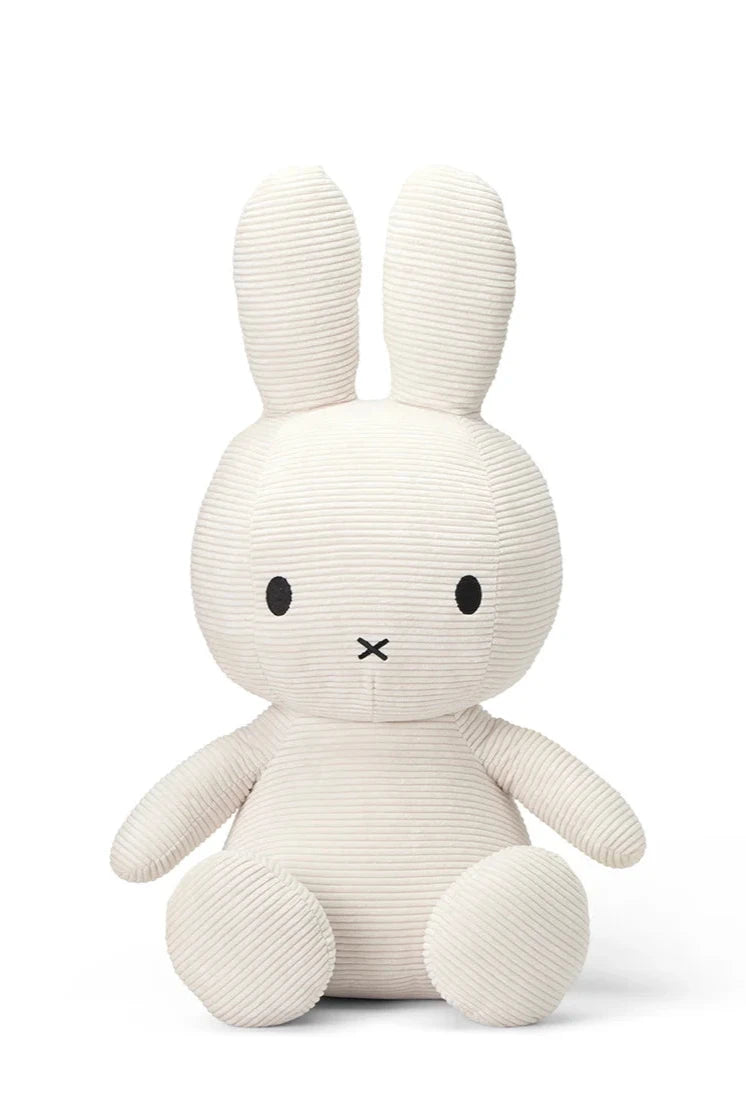 The Miffy ECO Corduroy Off White 50cm plush toy by BON TON TOYS X MIFFY is a charming, off-white rabbit with long ears, round black eyes, and a small stitched 'X' mouth. This adorable stuffed toy, perfect for cozy hugging sessions, is crafted with recycled PET filling to ensure eco-friendly fun. It sits gracefully against a plain white background.
