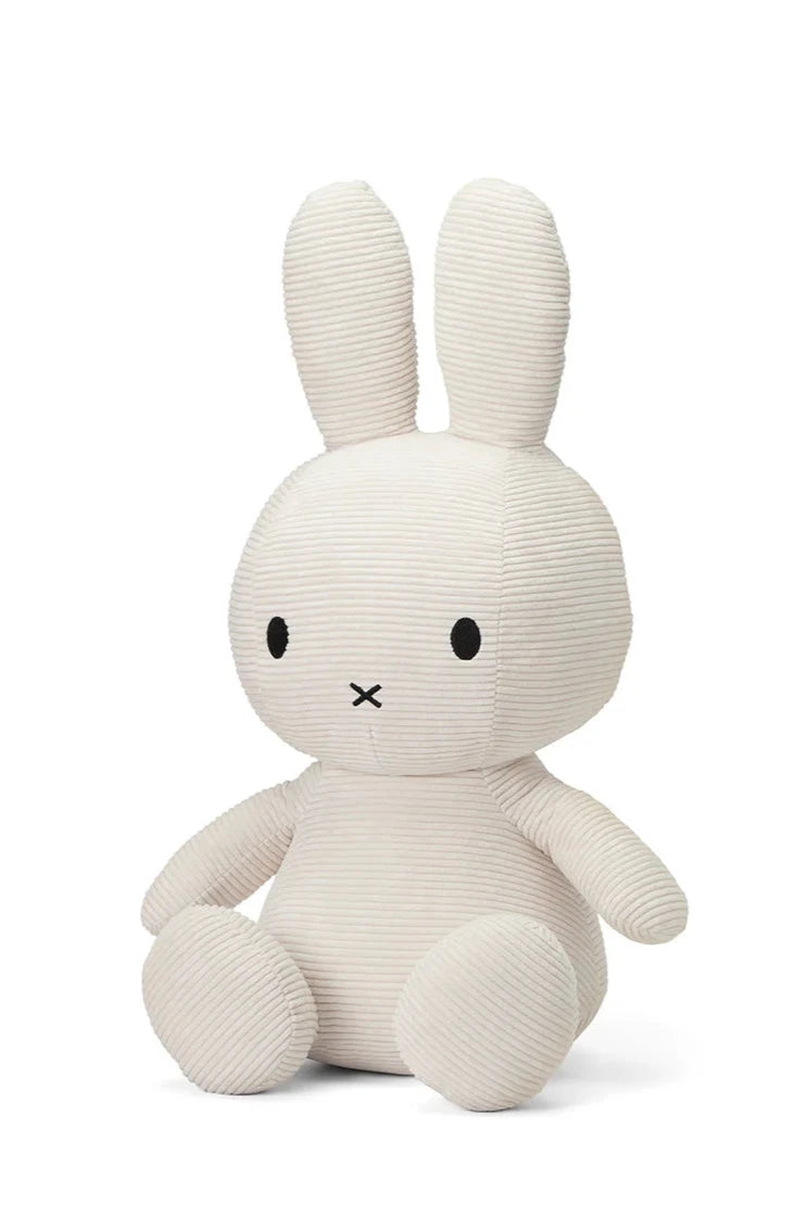 Introducing the Miffy ECO Corduroy Off White 50cm by BON TON TOYS X MIFFY: a delightful white rabbit featuring long ears, black eyes, and a small X-shaped mouth. Seated with its legs slightly apart, this plush toy offers a cozy ribbed texture and an eco-friendly touch with its recycled PET filling. The background is plain white.