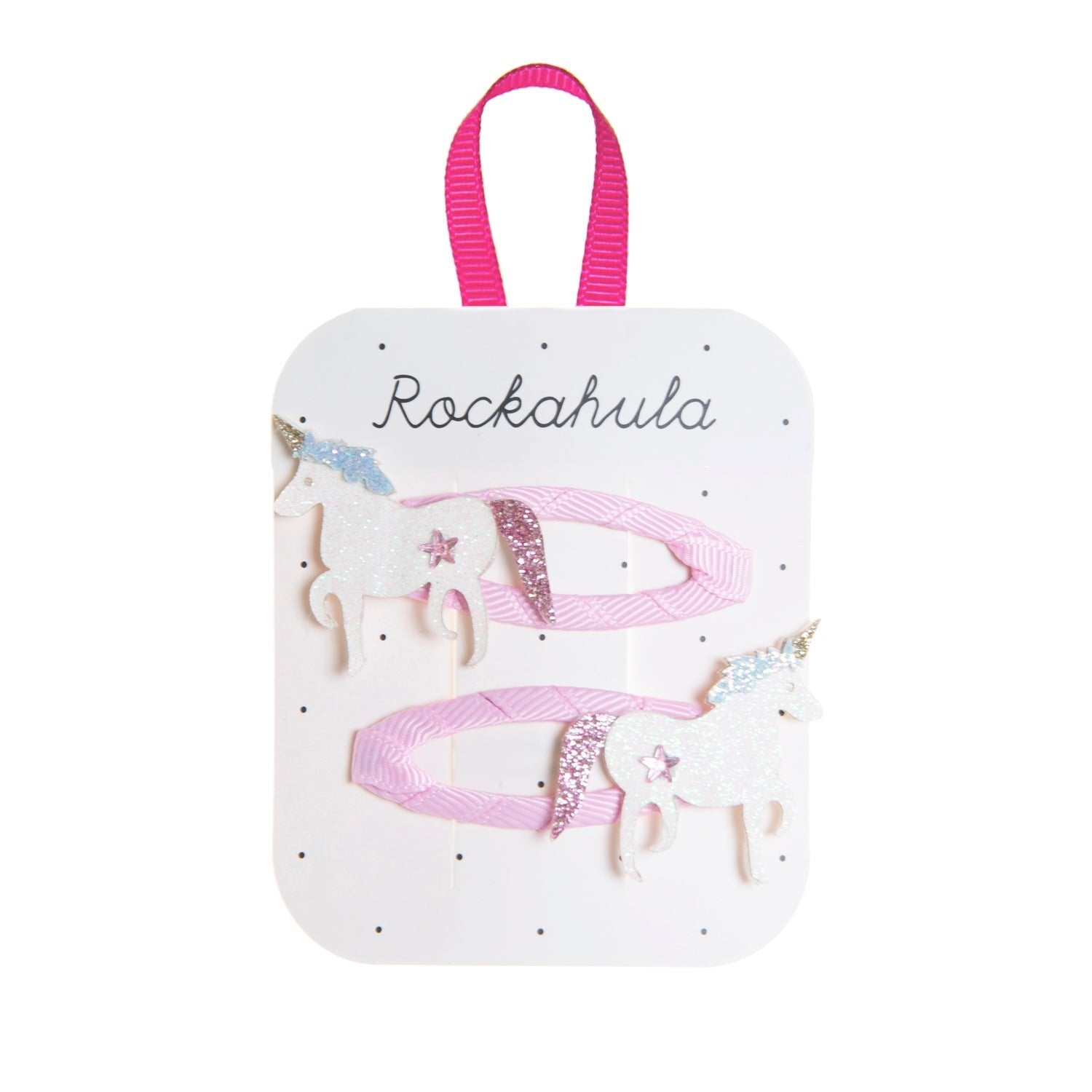 The ROCKAHULA Rockahula - Unicorn Clips set features two pink ribbon hair clips, each with a glittery white unicorn, gold horn, and pastel accents. The clips are displayed on a branded card with a bright pink loop at the top.