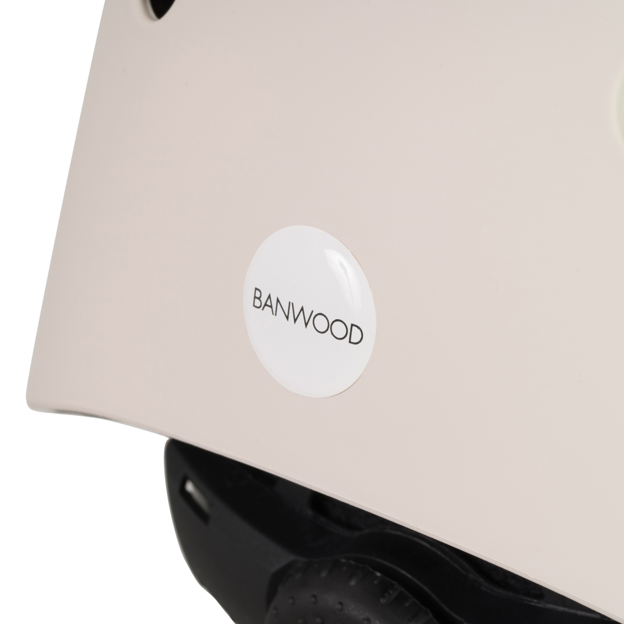 Close-up of a Banwood - Eco Helmet Ivory with a round "BANWOOD" logo. Its curved shape and chin strap reflect its safety focus, crafted from durable recycled ABS materials for sustainability.