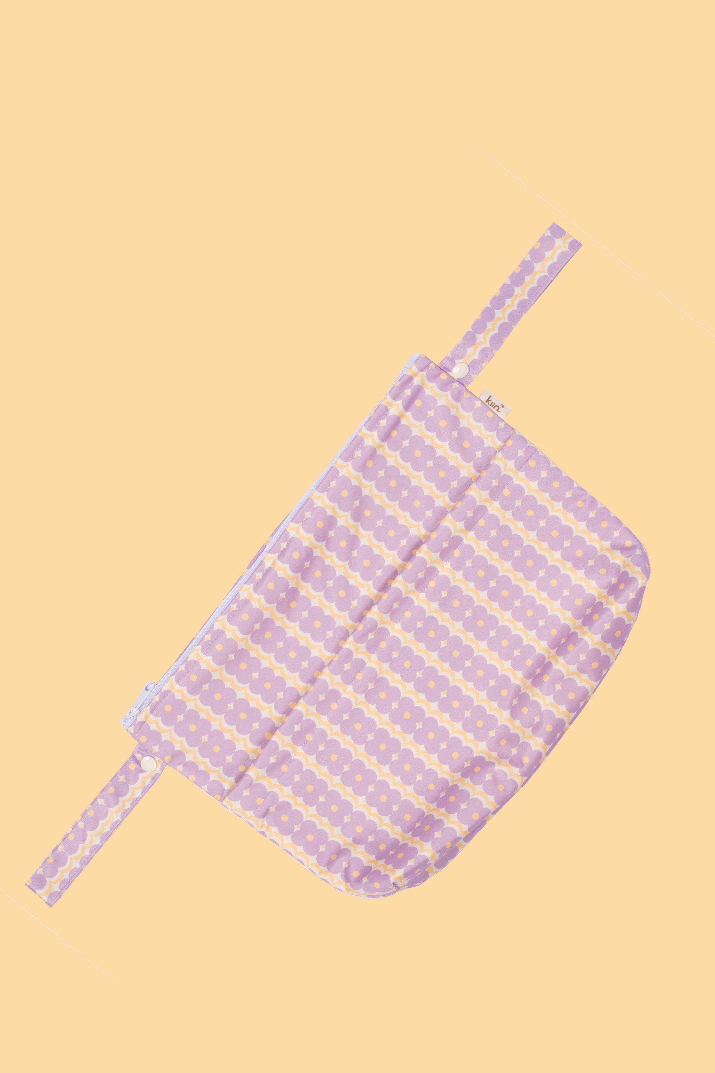 The KIIN BABY Reusable Wet Bag Flower Power is a pink and white patterned fabric bag featuring a zipper and side handles. Displayed against a peach background, it showcases an eco-friendly floral design, ideal for use as a wet bag.
