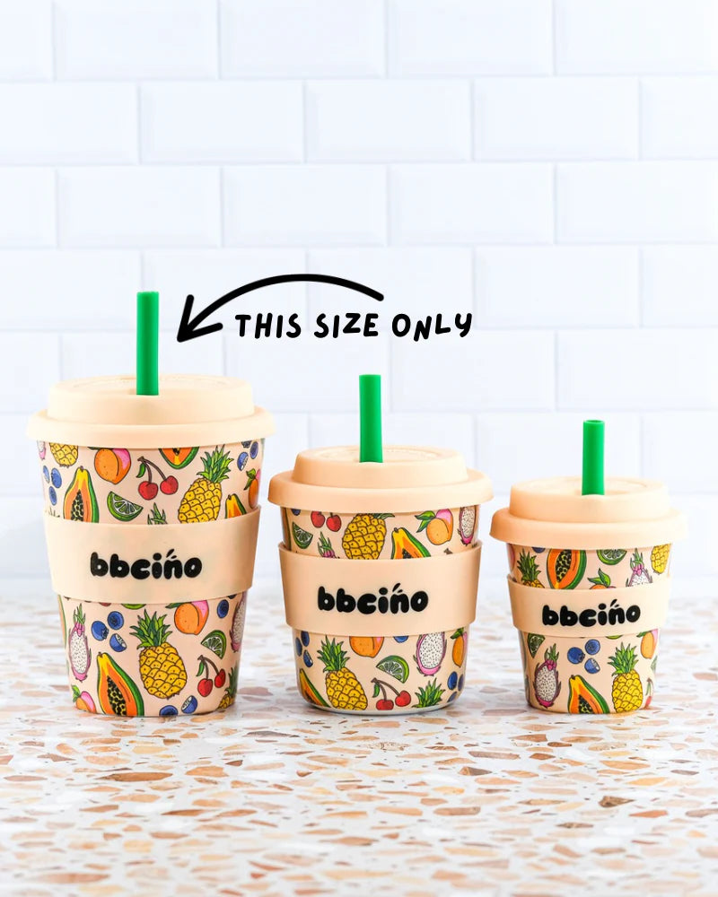 Three limited edition BBcino BiggieCino 350ml reusable cups with fruit patterns and green straws sit on a counter. An arrow labeled "THIS SIZE ONLY" points to the largest eco-friendly cup—all with beige lids and "BBcino" bands.