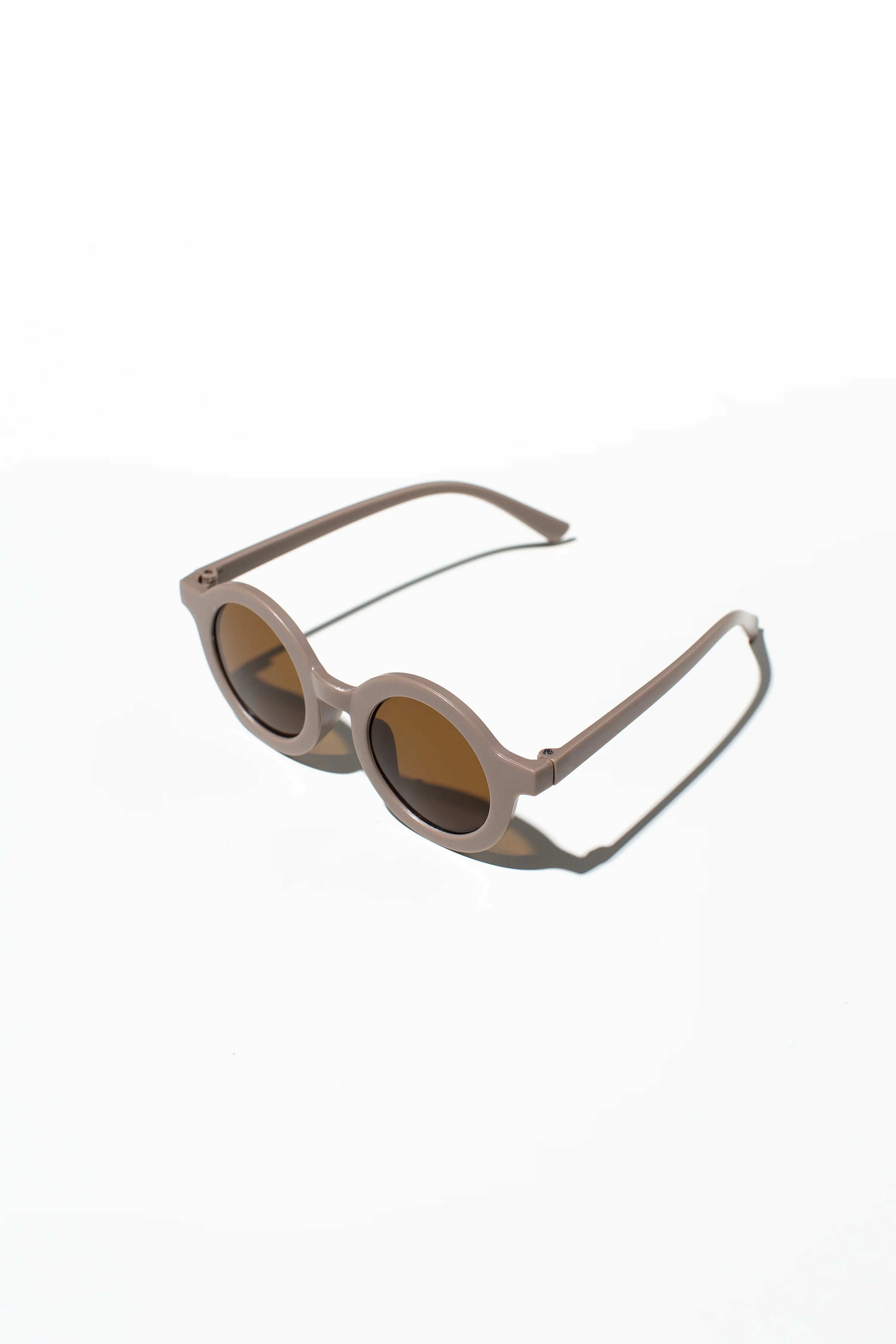 The Kids Shades Biscuit by LITTLE DROP are round, beige sunglasses with brown lenses on a crisp white background. The minimalist shadows add style, and the UV400 protection keeps young eyes safe.
