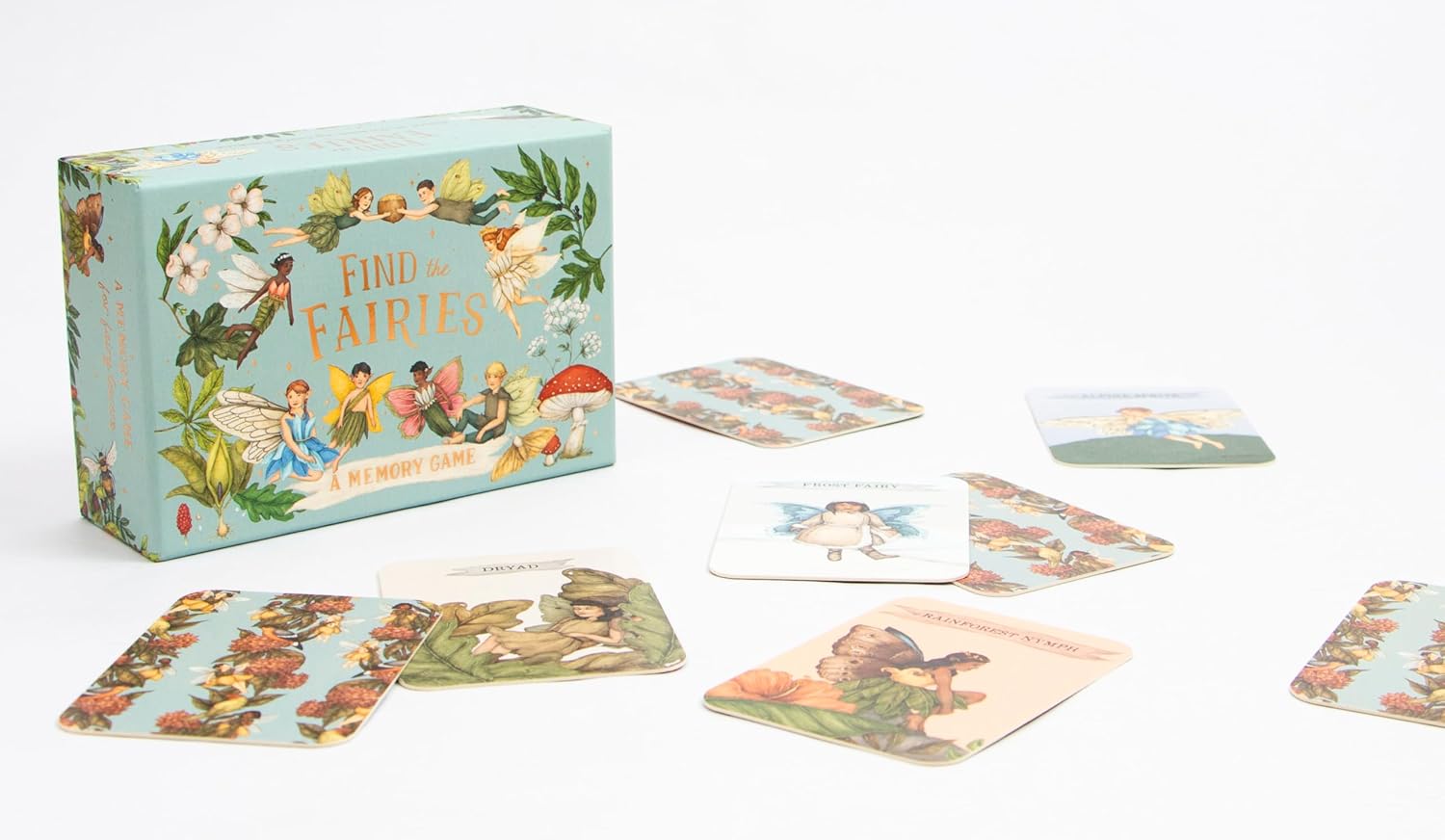 A box of BAY KIDS' "Find the Fairies: A Memory Game" rests beside vibrant, fairy-themed cards on a white surface, displaying colorful illustrations of diverse fairy species and nature scenes.