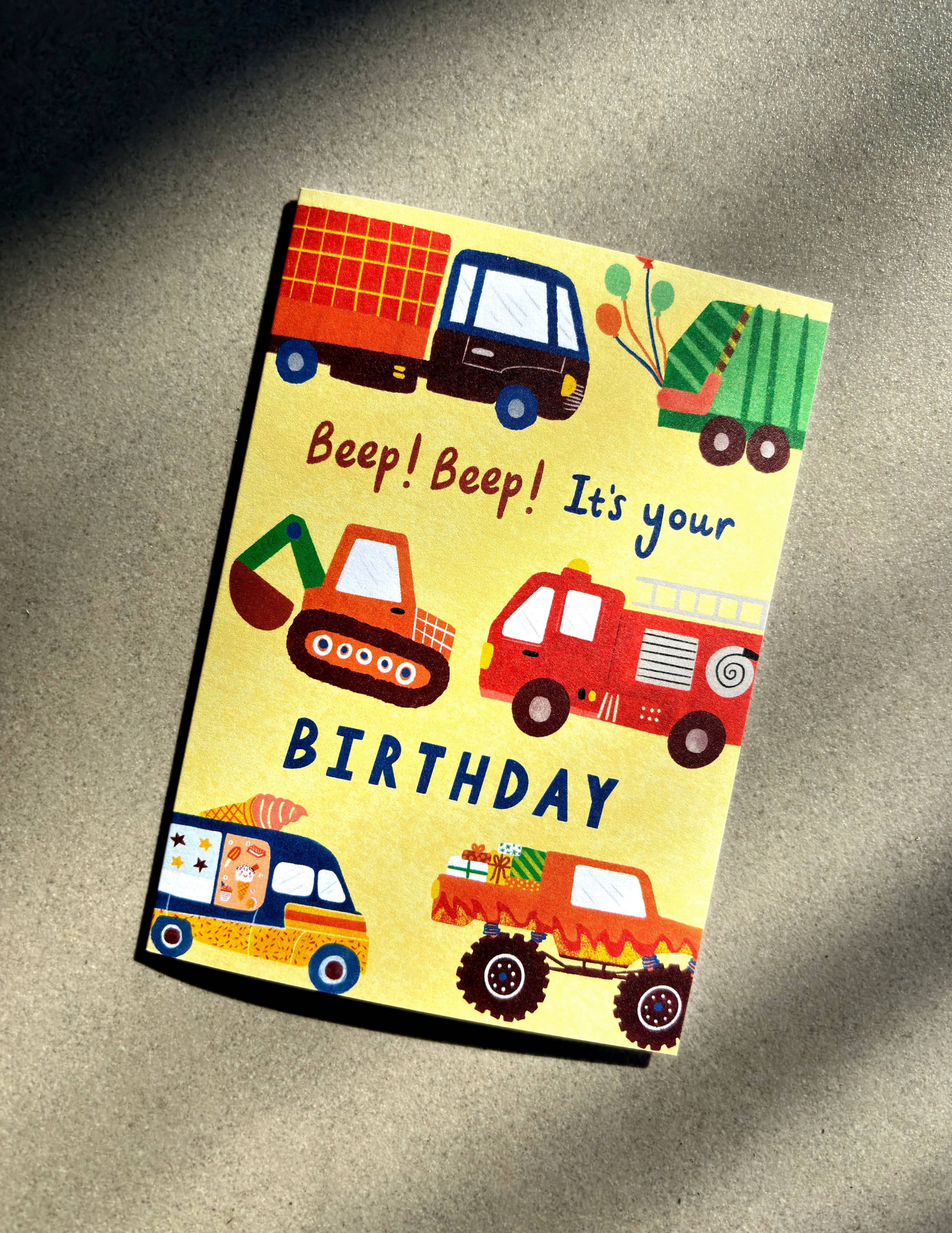 The Vehicles Happy Birthday Card from Lauren Sissons Studio is a vibrant birthday card on recycled paper, featuring illustrations of vehicles such as a truck, fire engine, monster truck, and ice cream van. Ideal for vehicle lovers, it presents the message "Beep! Beep! It's your BIRTHDAY" against a bright yellow background.