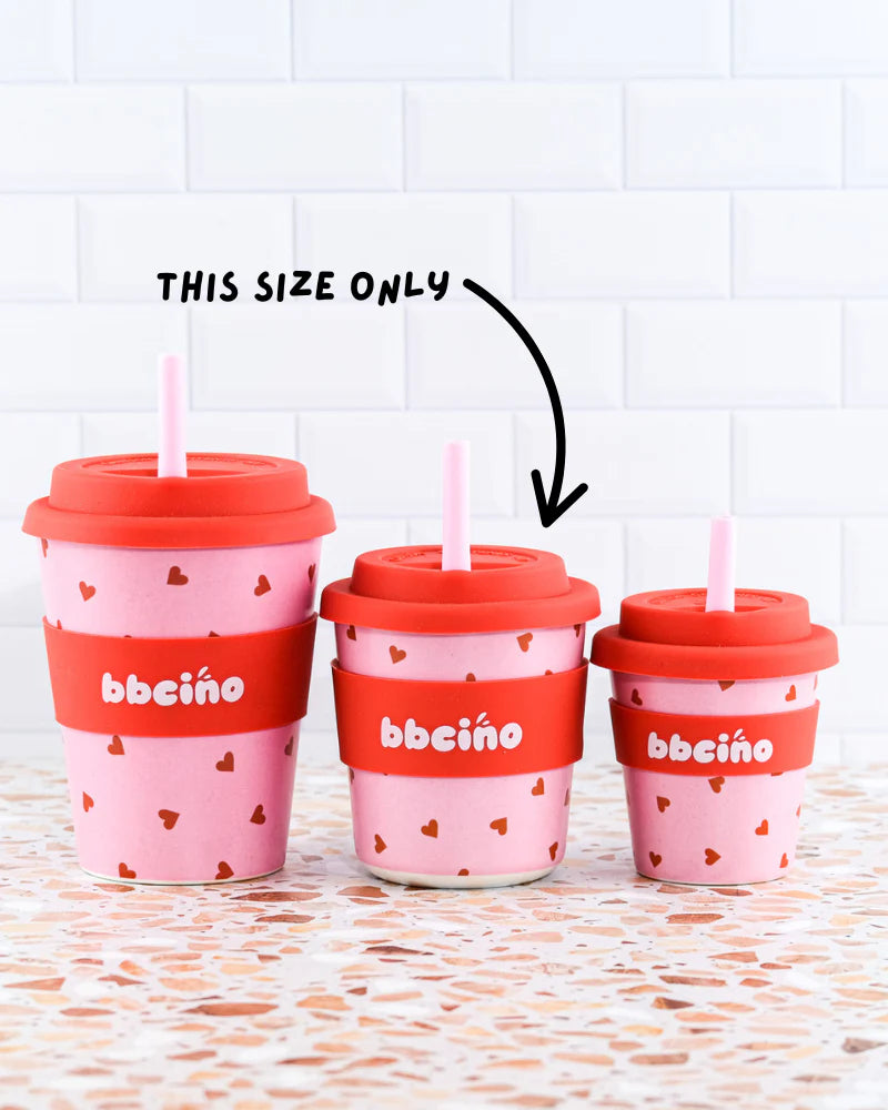Three BBCINO reusable BambinoCino cups with heart patterns and red lids are lined up by size. An arrow highlights the middle 240ml “Sweetheart” cup, branded “bbeüno”—an eco-friendly choice.