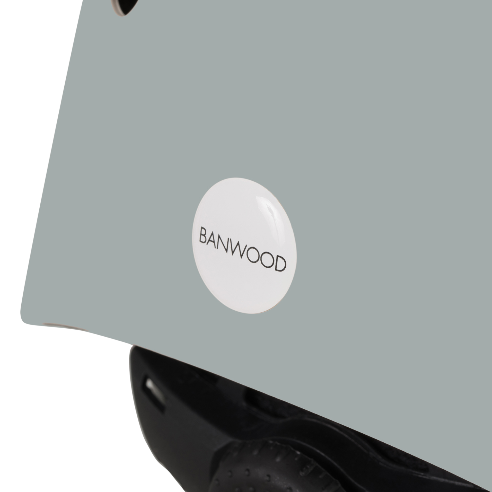 Close-up of a Banwood - Eco Helmet Clay in light gray with the "BANWOOD" logo on a white circular sticker. Made from recycled materials, it highlights safety and sustainability with its black adjustment dial and crafted edges.