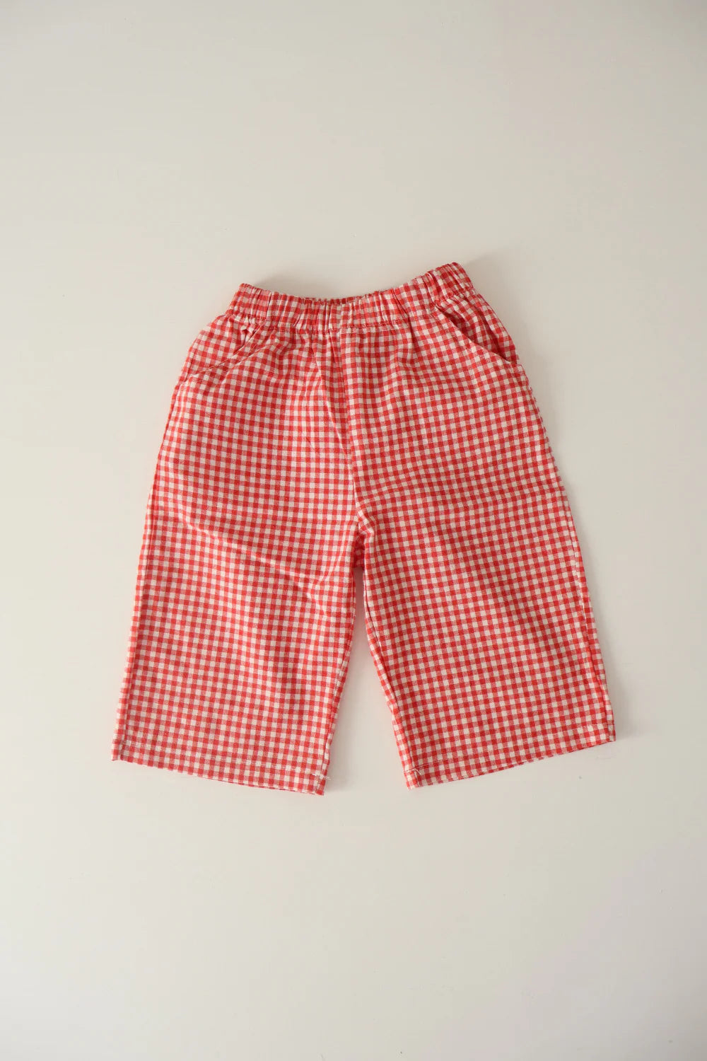 The WORN CURATIONS All Day Pant Chilli is a pair of unisex red and white cotton gingham pants with a comfy elastic waistband and two side pockets, wide-leg fit, and classic checkered pattern—perfect for children.