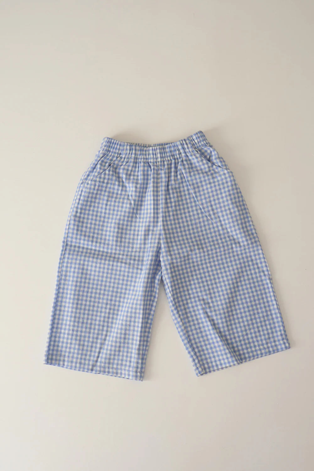 The WORN CURATIONS All Day Pant Cornflower features blue and white unisex gingham, a comfy elastic waistband, and soft cotton in a wide-leg kids’ style. Shown laid flat on a light background.