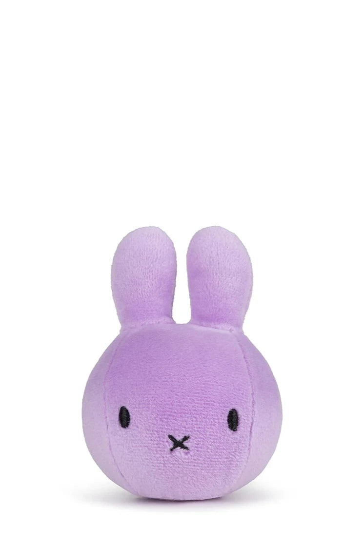The Miffy Squish Ball Lilac from BON TON TOYS X MIFFY is a round, purple plush resembling a rabbit with upright ears, small black eyes, and an "X" stitched mouth. Perfect for stress relief, this cute toy is displayed against a plain white background.