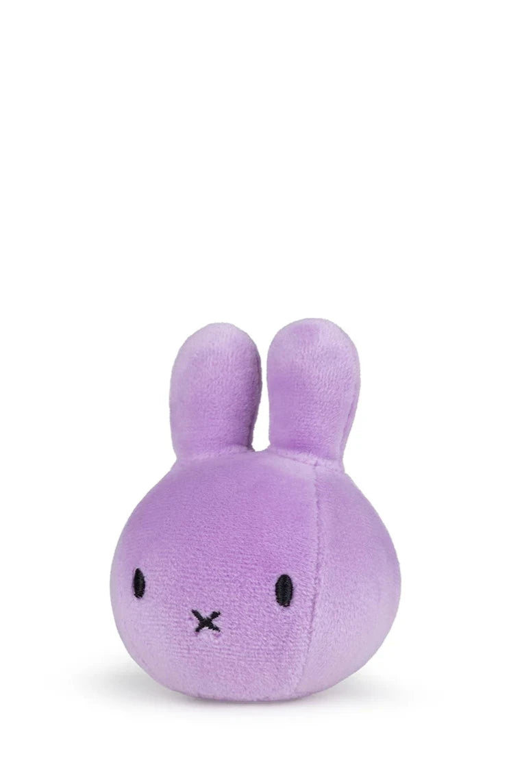 The Miffy Squish Ball Lilac from BON TON TOYS X MIFFY is a small, plush toy resembling a rabbit with round features. Made of soft purple fabric, it has simple black embroidered eyes and a tiny "X" for a mouth, ideal for stress relief. It sits against a plain white background.
