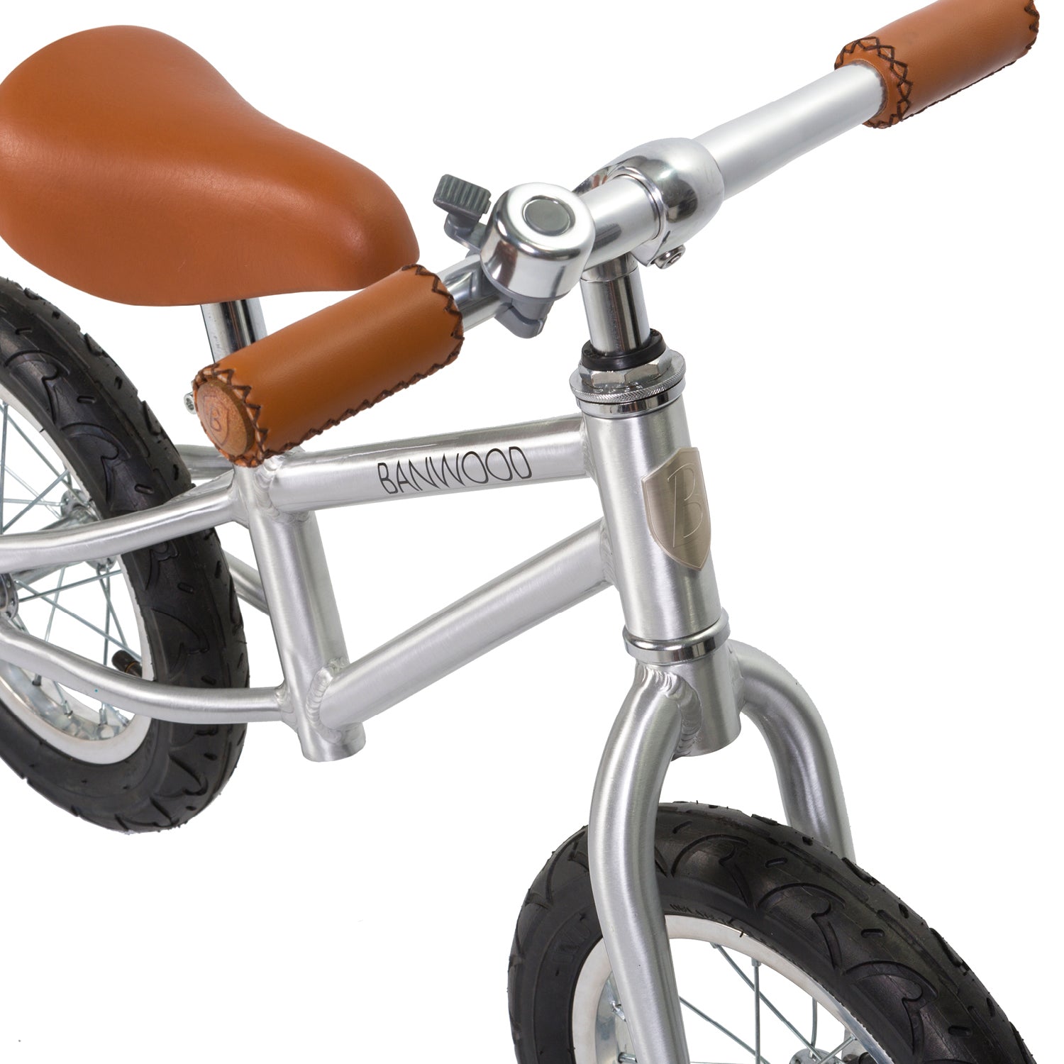Close-up of the Banwood Vintage Balance Bike Chrome: a silver frame with brown leather-like grips and saddle, black tires, and a metal bell on the handlebar. Ideal for beginners, featuring the BANWOOD brand elegantly printed on the frame.