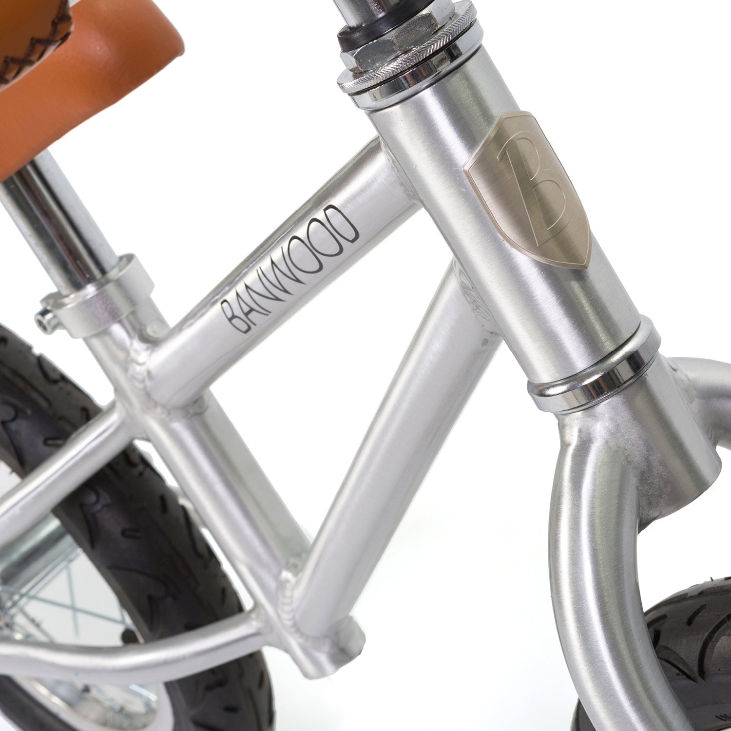 Close-up of the silver Banwood - Vintage Balance Bike Chrome frame, with "BANWOOD" branding. Ideal for novice cyclists, it features black tires and a peek of the tan synthetic seat, plus a metallic emblem on the front.