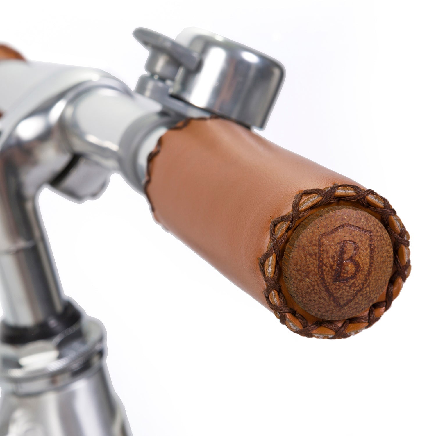 A close-up of a BANWOOD - Vintage Balance Bike Chrome handlebar shows a silver bell. The brown leather-wrapped vintage-style handle boasts braided details and an embossed "B" inside a shield on the end cap, adding charm to any beginner cyclist's ride.