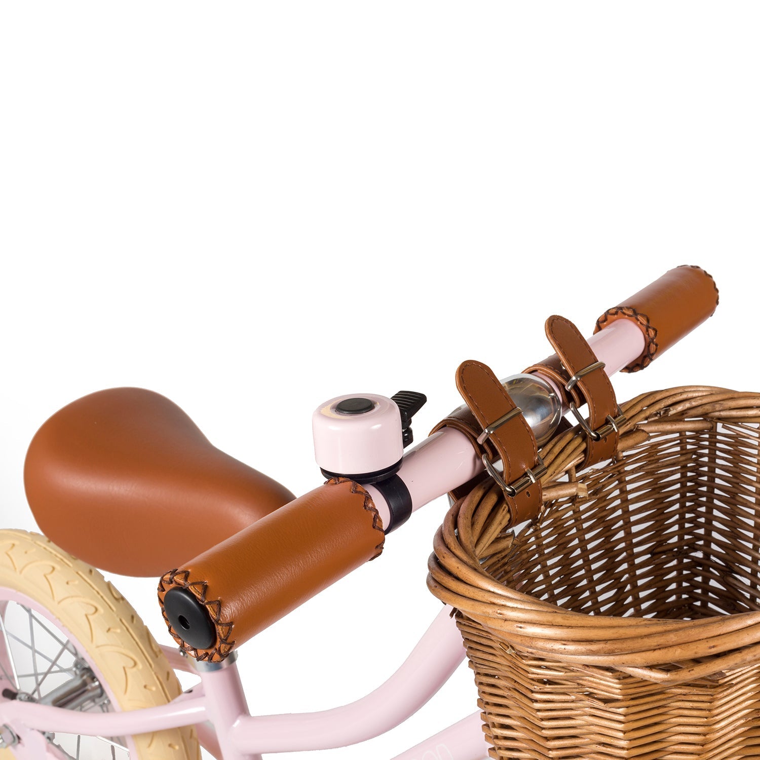 Close-up of the Banwood - Vintage Balance Bike Pink handlebar featuring brown leather grips, a pink frame, and a wicker basket. A white bell and tan saddle complement the cream-colored tires. From BANWOOD brand.