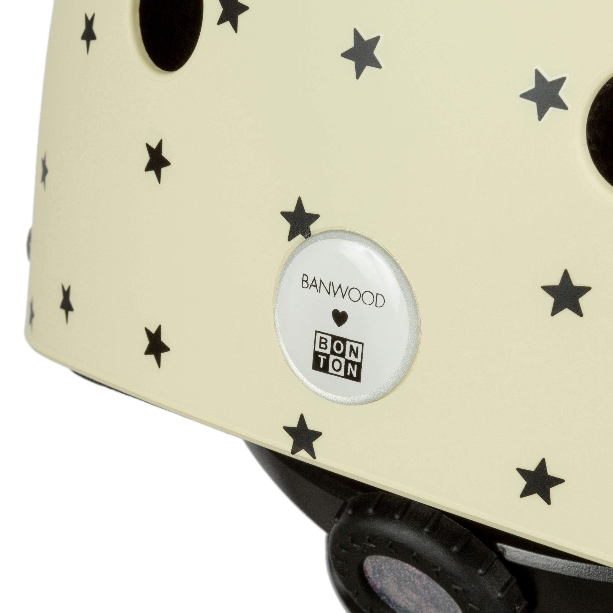 This children's bike helmet, "Banwood - Bonton x Banwood Helmet Cream - S," features a beige background with black star patterns and a circular logo reading "BANWOOD" and "BON TON." It offers maximum protection and has an adjustable size for growing kids.