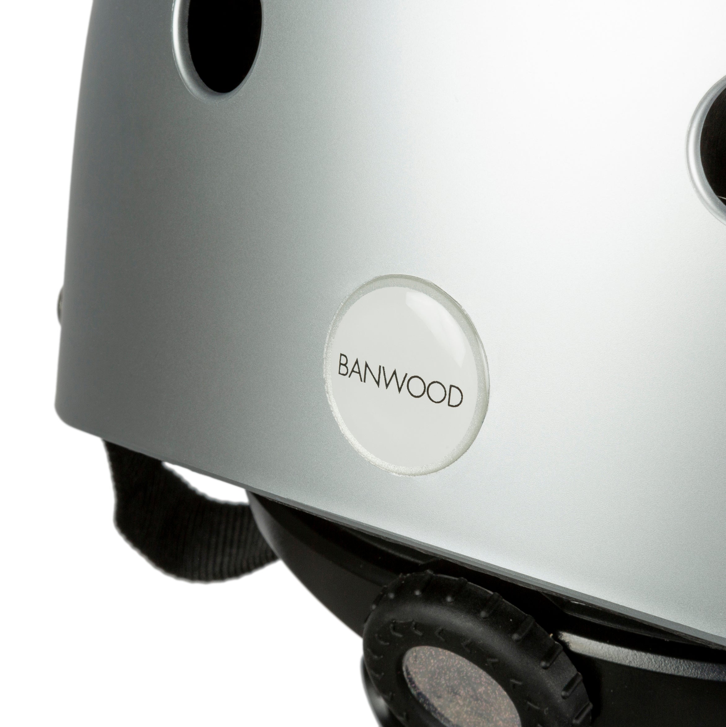 Close-up of the Banwood - Classic Helmet Chrome - S, featuring ventilation holes and "BANWOOD" branding. A black adjustable strap and fitting dial complete this silver helmet, perfect for young riders seeking style and safety.
