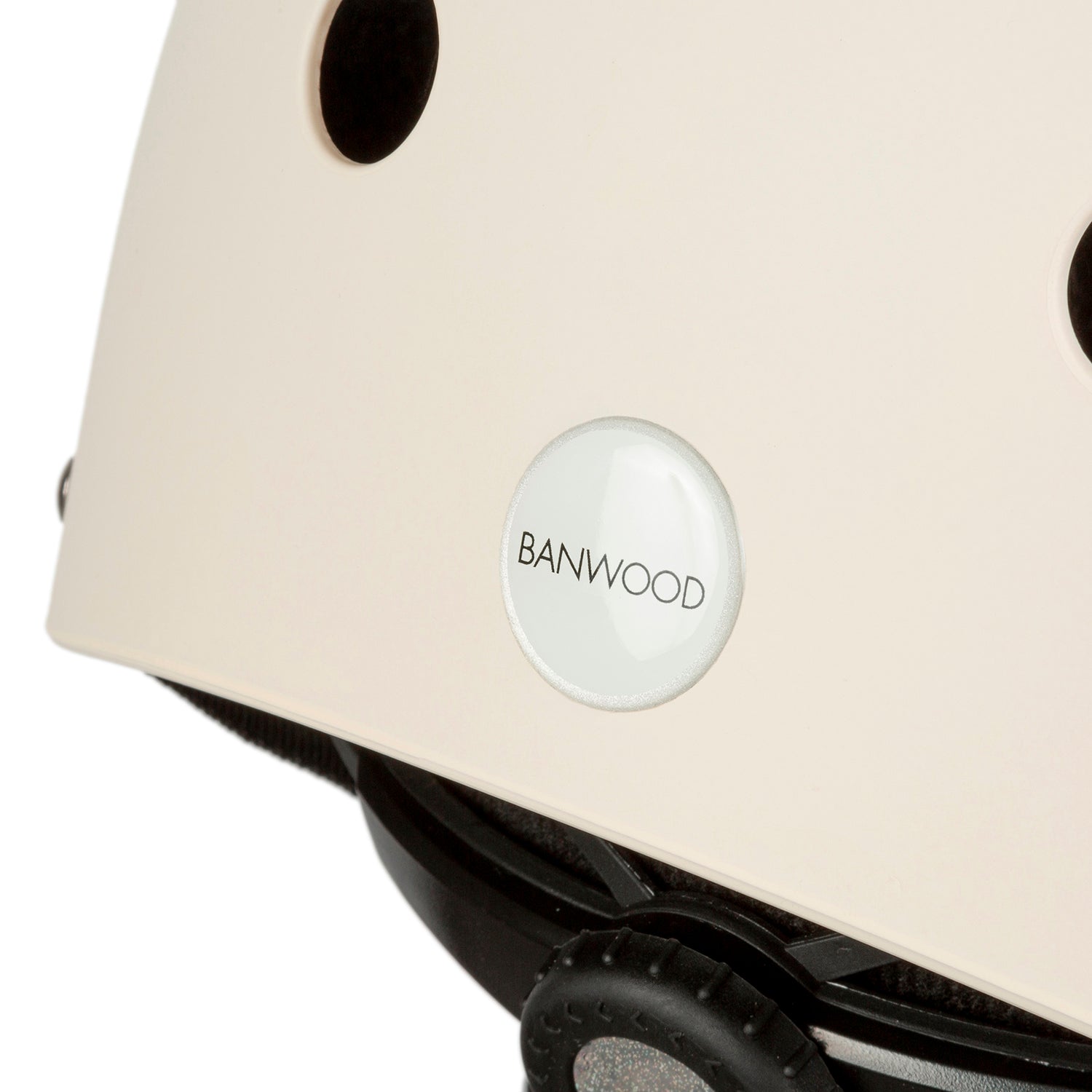 A close-up of the Banwood Classic Helmet Cream - S, shows ventilation holes and a "BANWOOD" badge. The adjustable straps and buckle provide a snug fit, making it an ideal kids' bike helmet.
