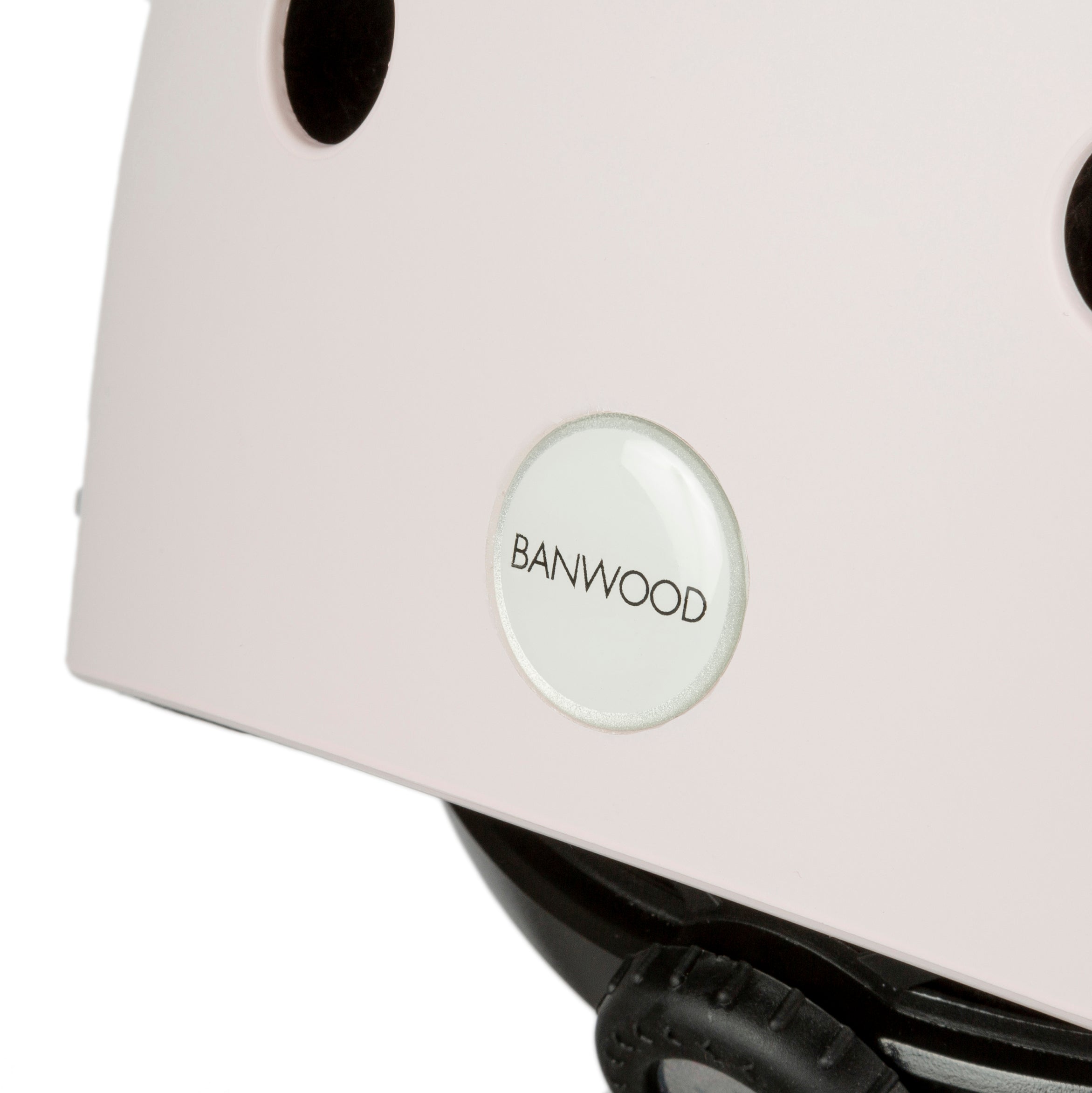 Close-up of the Banwood - Classic Helmet Pink - S, ideal as a children's bike helmet. It has ventilation holes, a black strap, and BANWOOD's circular emblem.