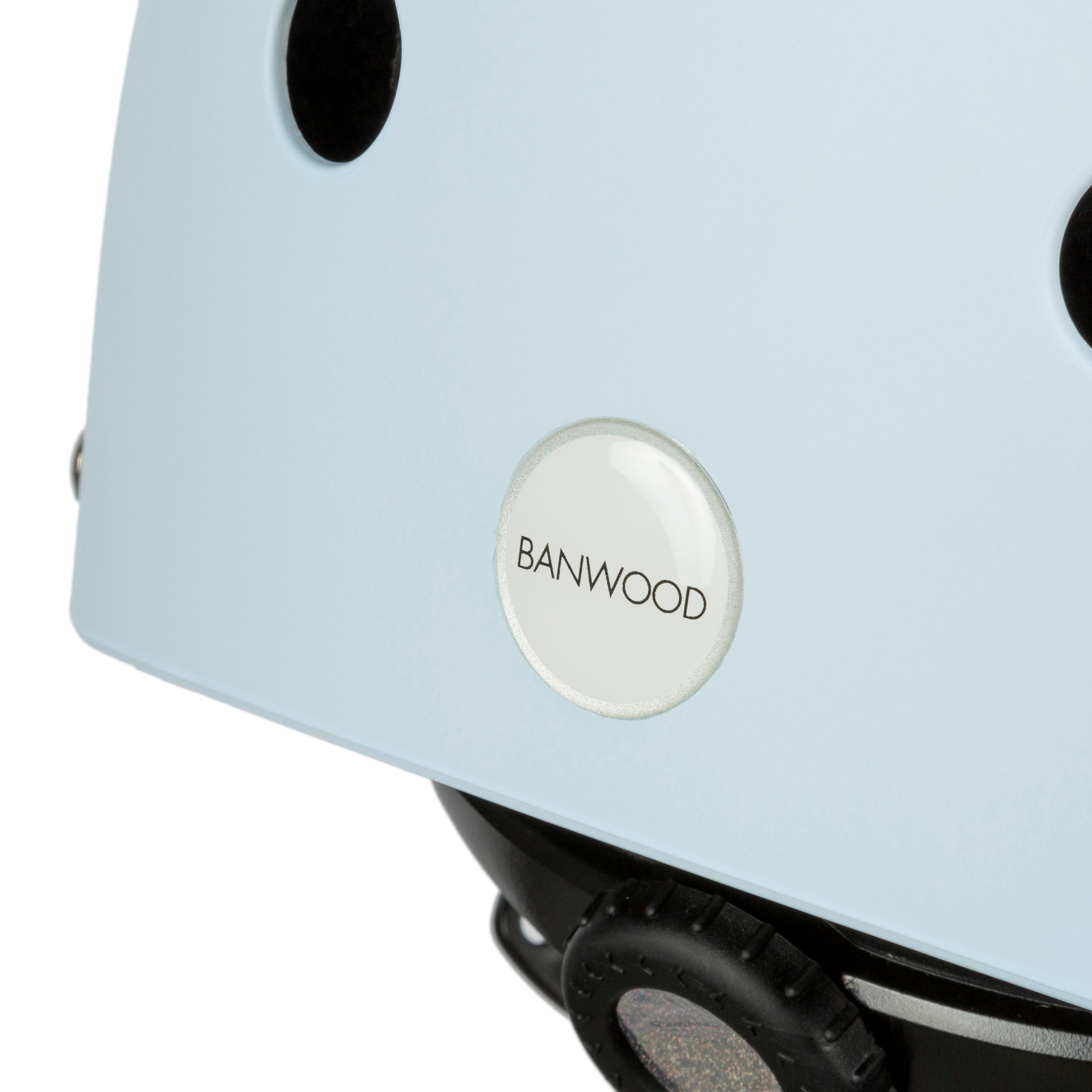 Close-up of a light blue kids helmet, Banwood - Classic Helmet Sky - S, featuring ventilation holes, a round "BANWOOD" button, and an adjustable black strap.