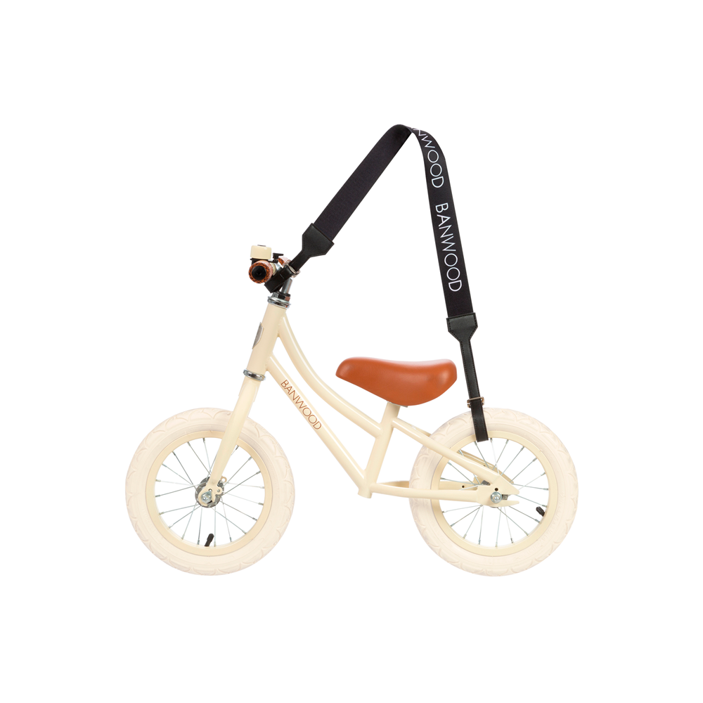 The beige balance bike, with white wheels and a tan seat, comes with a black Banwood Carry Strap that displays the BANWOOD name. A small bell on the handlebar adds style and function for young riders.