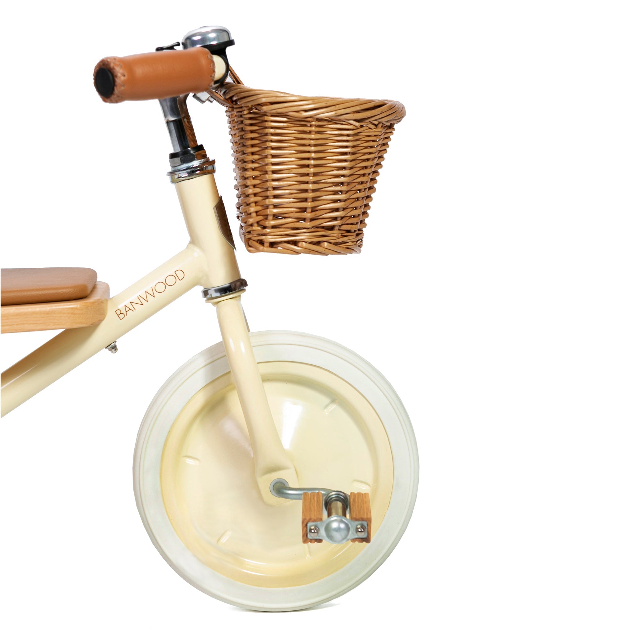 A close-up of the Banwood - Trike Cream, a child's balance bike by BANWOOD, showcasing its cream color, charming wicker basket on the front, brown seat and handlebars, smooth plastic front wheel, and wooden footrests.
