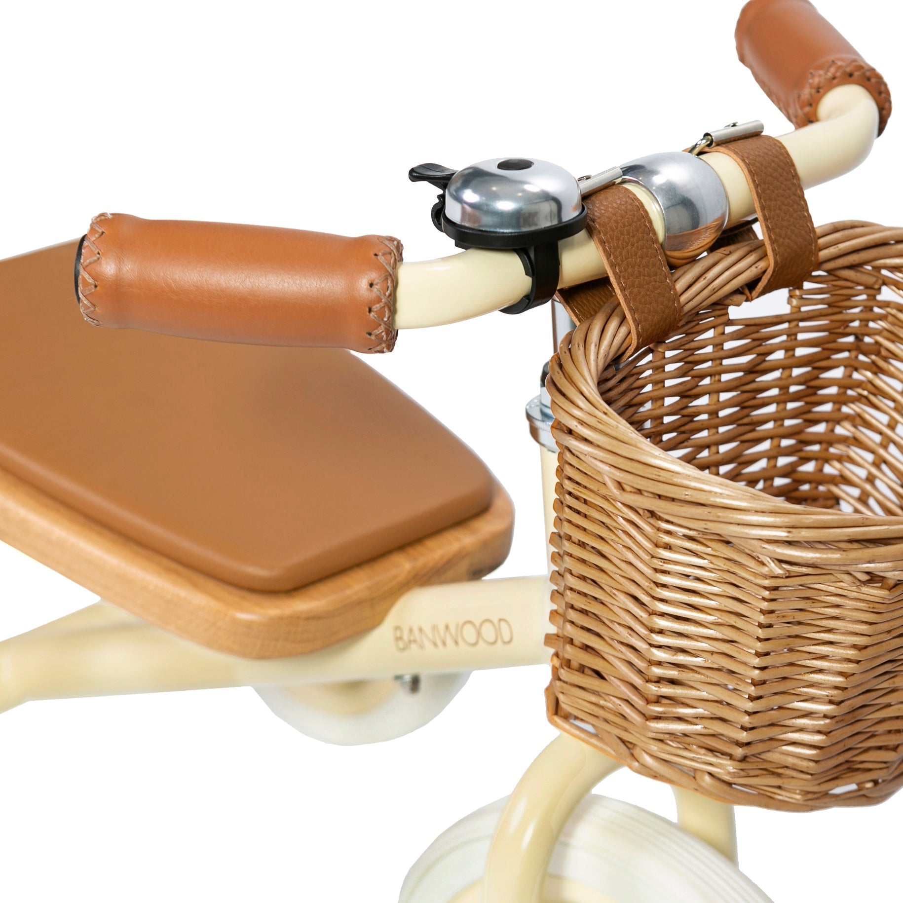 Close-up of the Banwood Trike Cream featuring a beige color with brown seat and grips. The handlebars have a small bell and charming wicker basket for treasures. "BANWOOD" adorns the frame, making this tricycle both stylish and playful for kids.