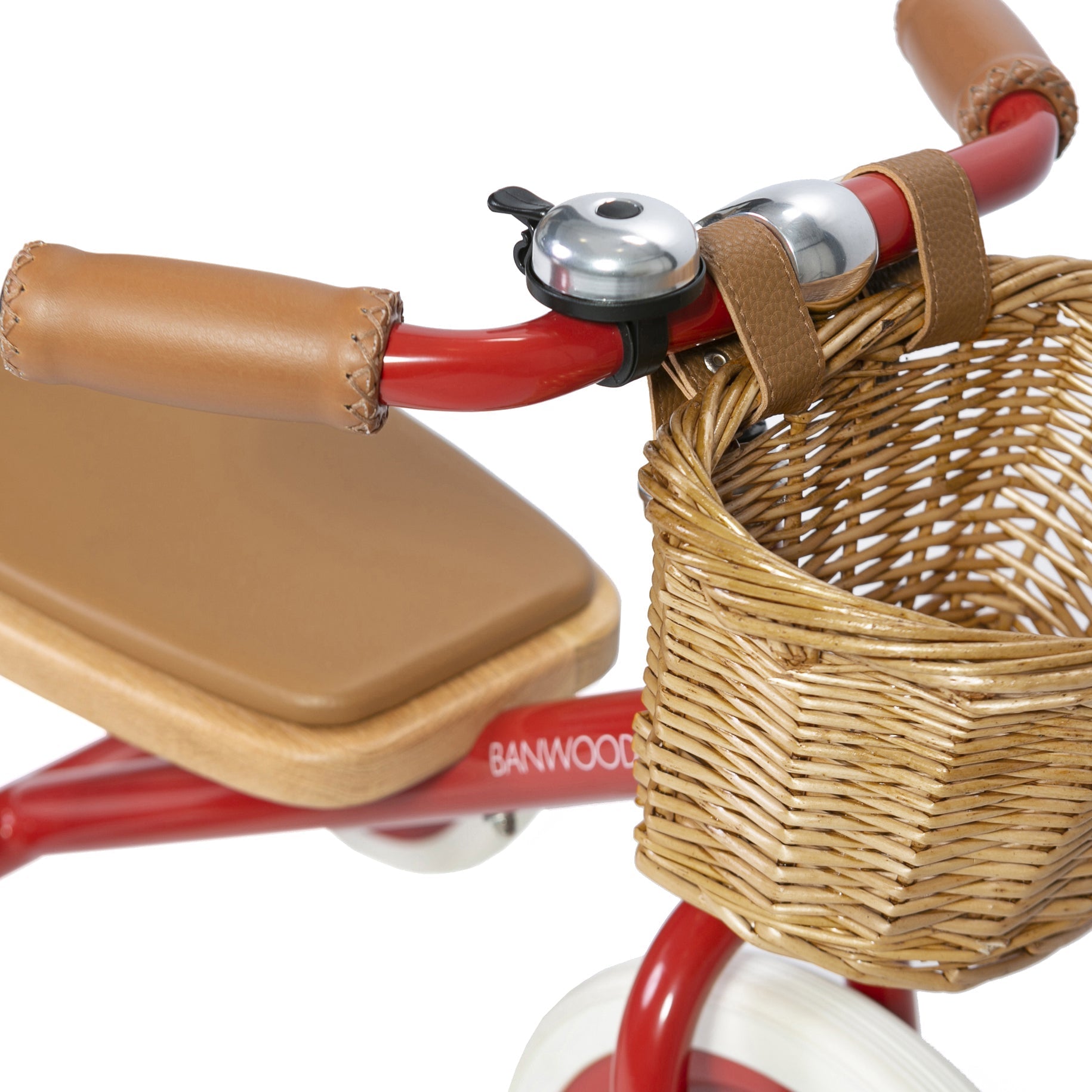 Close-up of the Banwood - Trike Red by BANWOOD, featuring a red handlebar with a built-in wicker basket, brown leather seat and grips, and a silver bell. A wooden deck at the back ensures it's perfect for little adventurers.
