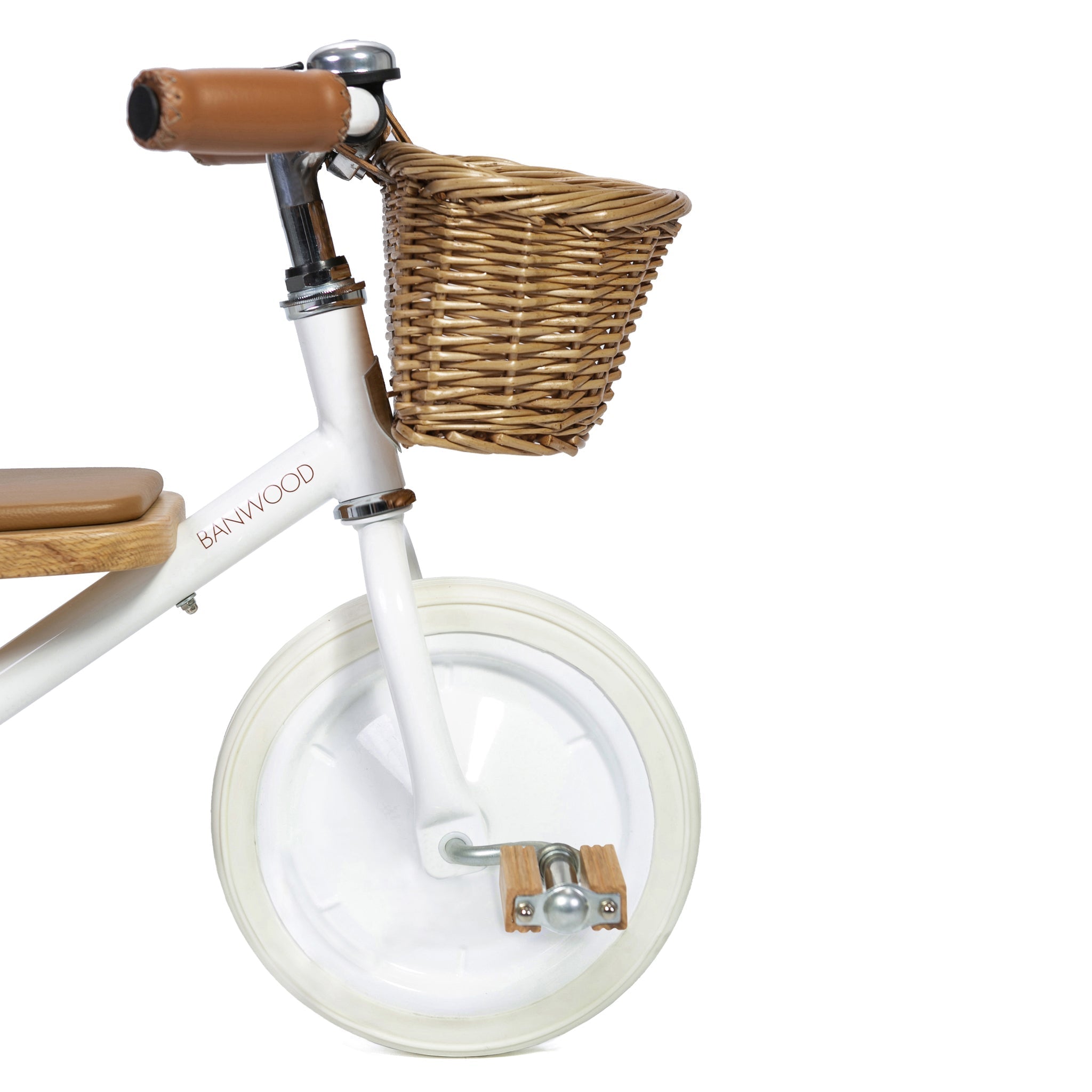 Close-up of the Banwood - Trike White, a children's balance bike with a wicker basket, brown grips, a wooden seat, and clear wheels. The frame subtly displays the BANWOOD brand name, and a detachable push handle converts it into an adaptable baby trike.