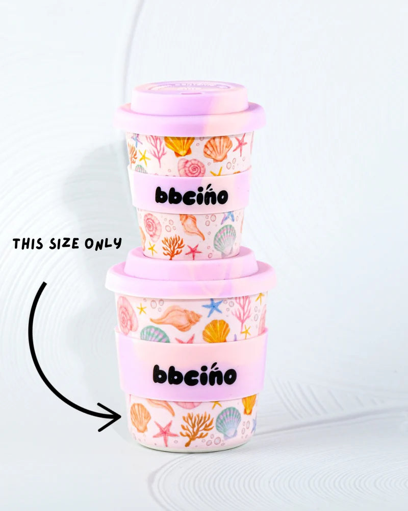 Two stacked reusable 240ml cups, crafted from sustainably farmed bamboo, feature pink lids and sleeves with colorful shell and starfish patterns. The larger cup says "THIS SIZE ONLY." Both eco-friendly cups proudly display the BBCINO brand name.