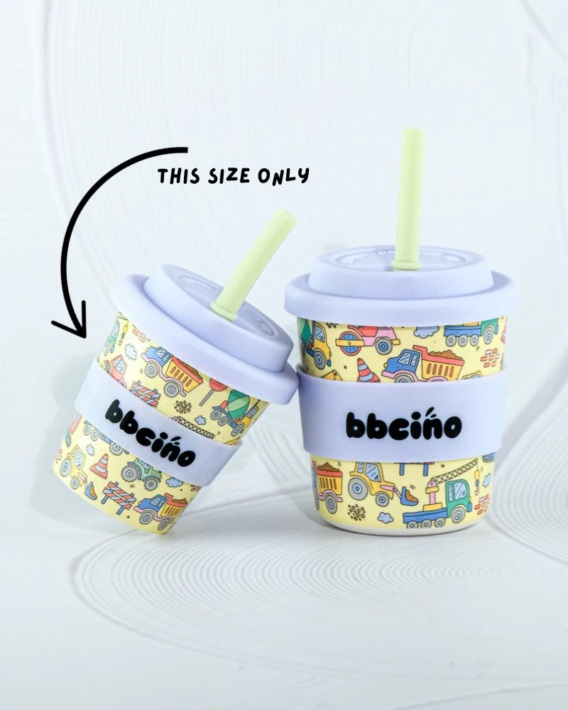 Two eco-friendly BBcino reusable cups are shown: a larger cup labeled "BBcino" and a smaller 120ml "Dig It" cup. Both have pastel lids, straws, and colorful vehicle designs. The smaller cup is marked with an arrow saying "THIS SIZE ONLY." They're displayed on a textured white surface.