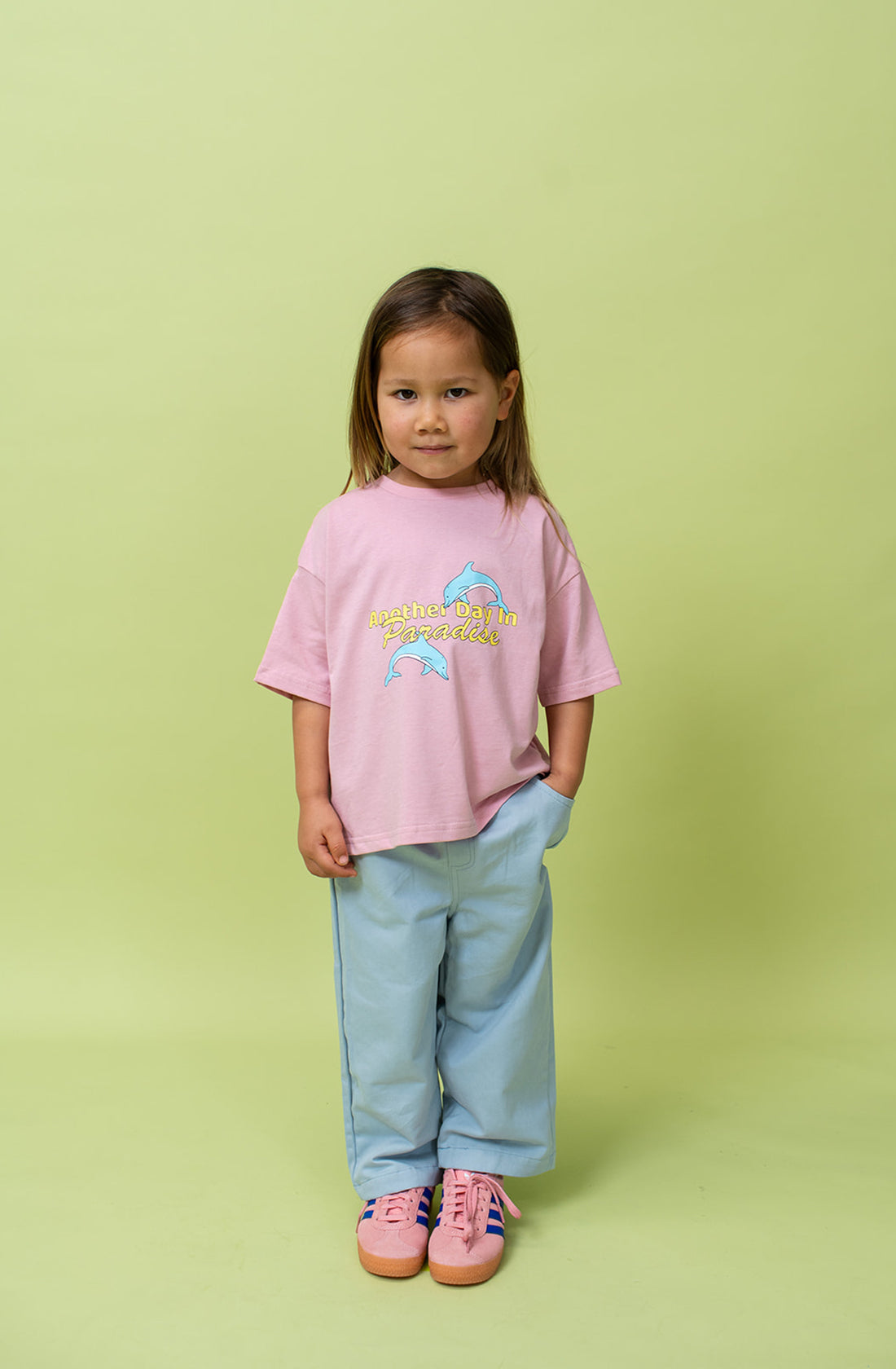 A young kid wearing the Lenn paradise tee in musk wearing blue pants and pink shoes.
