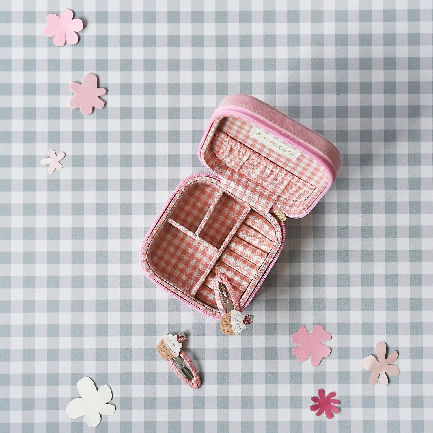 The Rockahula - Sweet Strawberry Square Jewellery Box by ROCKAHULA, in pink velvet with partitions, sits open on a gingham surface, surrounded by paper flowers and cupcake-shaped hair clips.