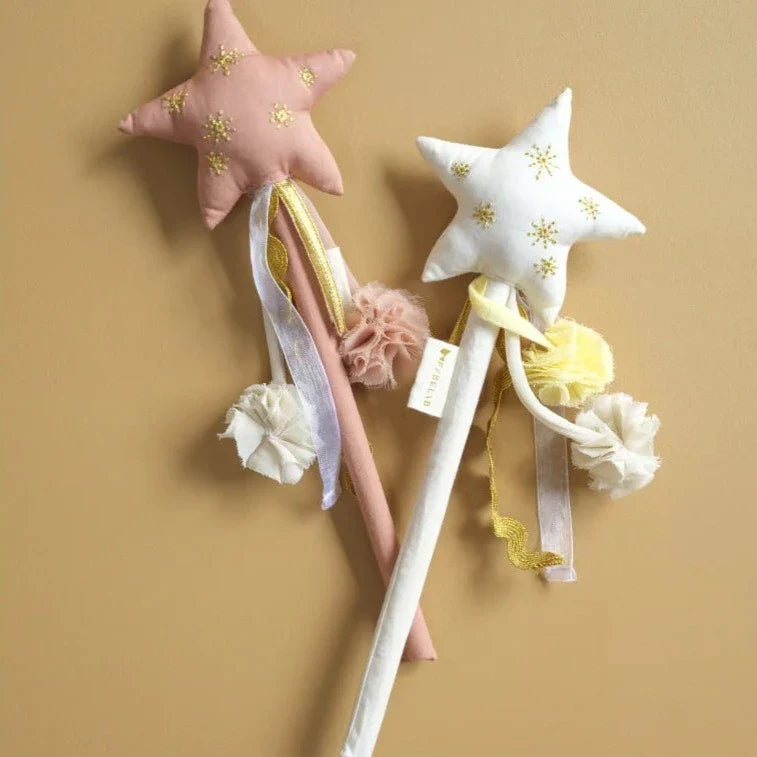Two Dress Up Magic Wand Naturals from FABELAB featuring long, white sticks adorned with ribbons and fabric pompoms. One wand has a pale pink star and the other a white star, both embellished with small, stitched gold stars. Perfect for costume play or to sprinkle some fairy dust, these wands are arranged on a beige background.