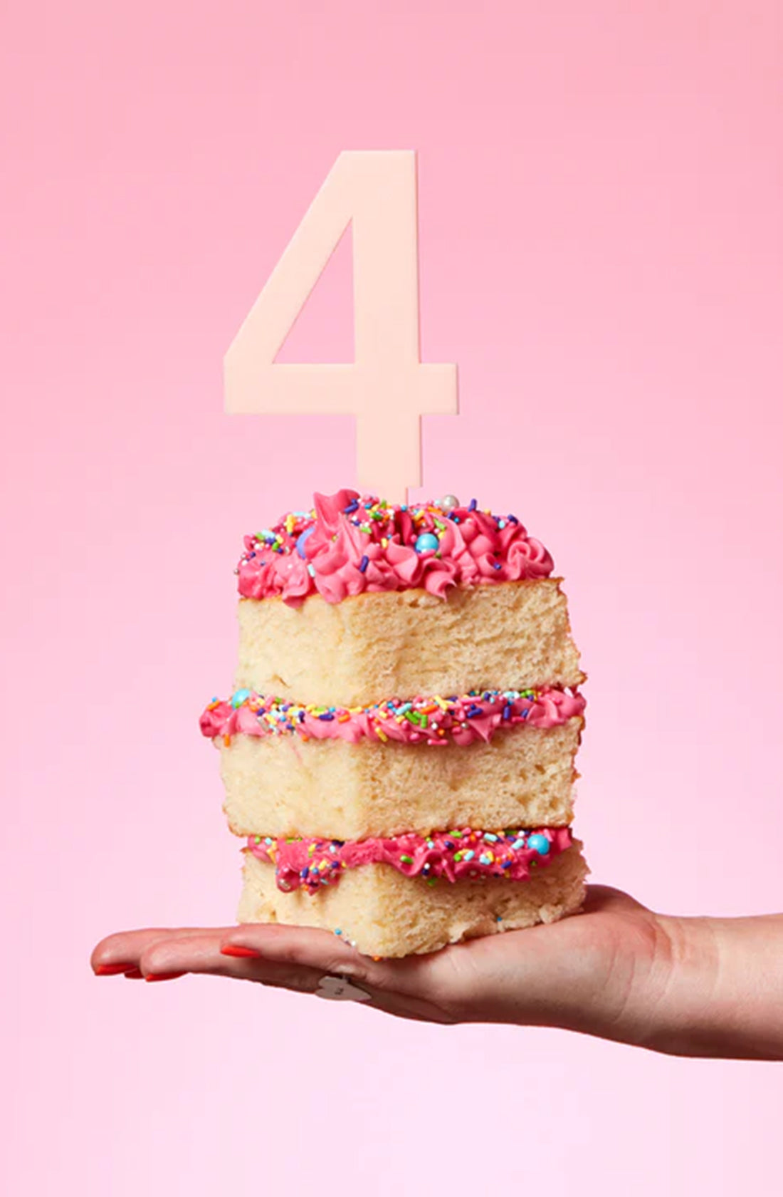 a HELLO KIT CO Large Cake Topper in Blush colour on top of a slice of cake with pink icing sugar and sprinkles in between the cake layers.