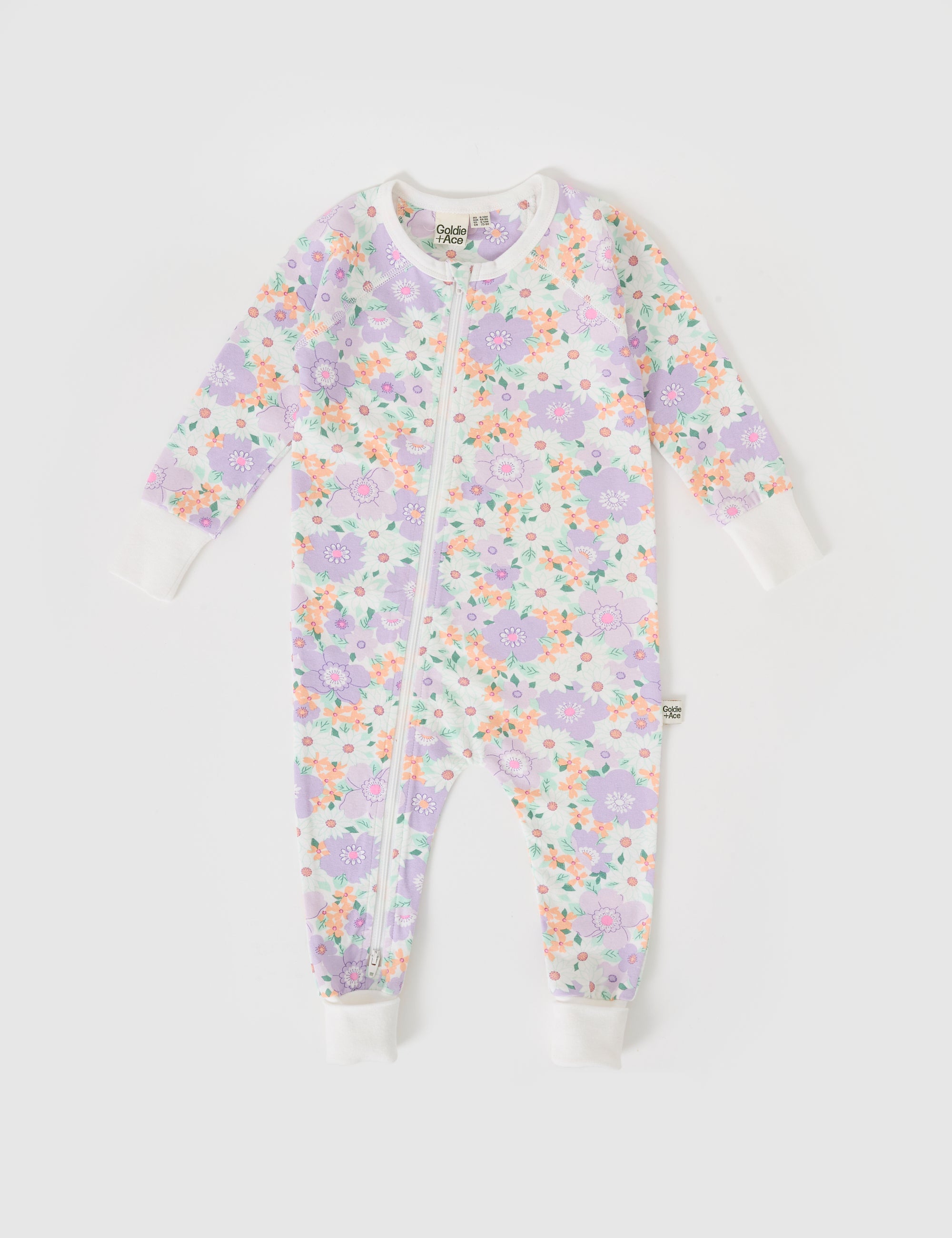 The Goldie + Ace Flora Zipsuit by GOLDIE + ACE is a baby onesie with long sleeves and legs, adorned with a colorful floral print of purple, pink, and orange flowers on white. It includes a two-way zip for easy changes and snug ribbed cuffs for comfort.
