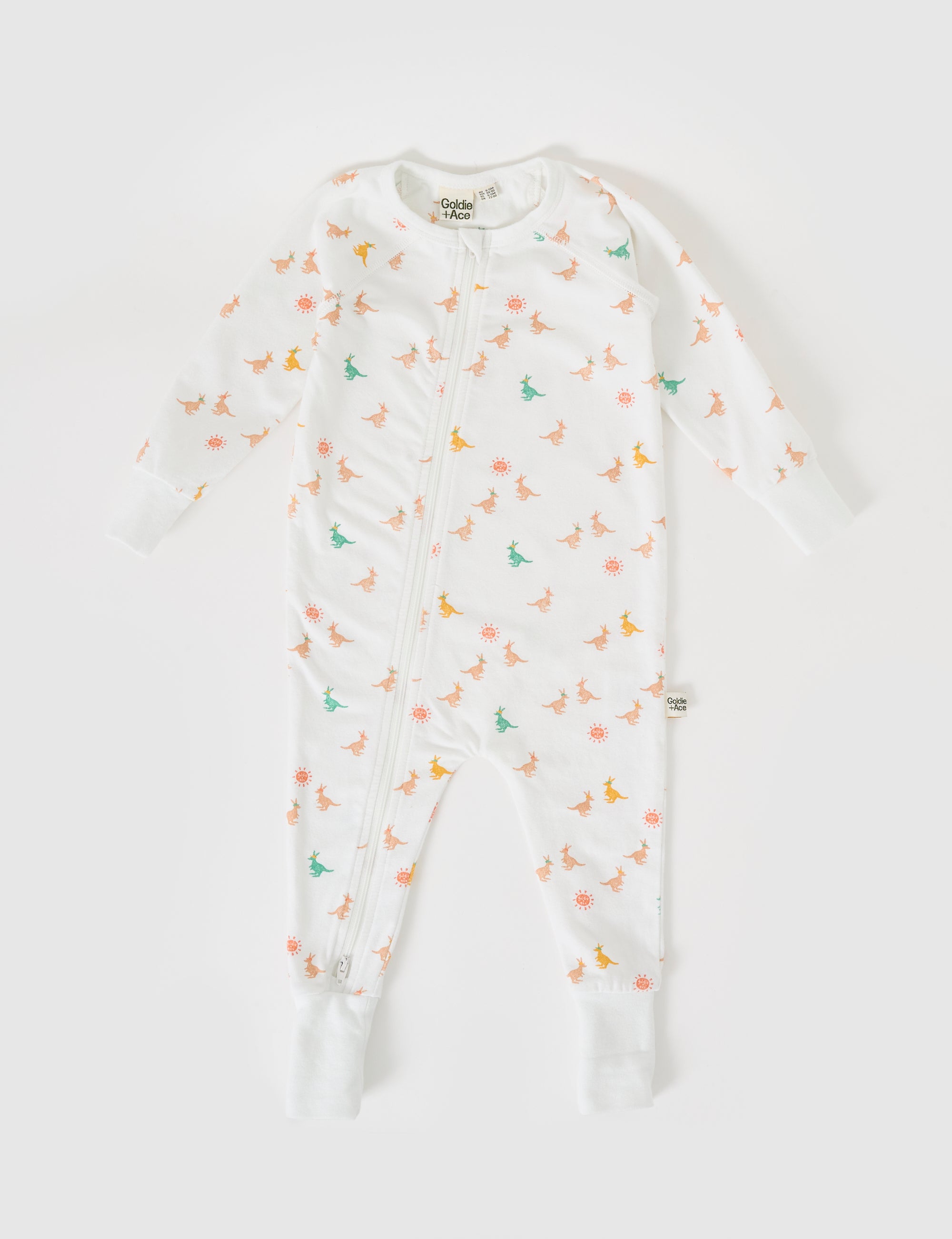 The Goldie + Ace Joey Zipsuit by GOLDIE + ACE is a white baby onesie with colorful dinosaur and sun prints. It features a two-way zip for easy changes, long sleeves, and extendable ribbed cuffs. Laid flat on a white background, it blends practicality with playful style.