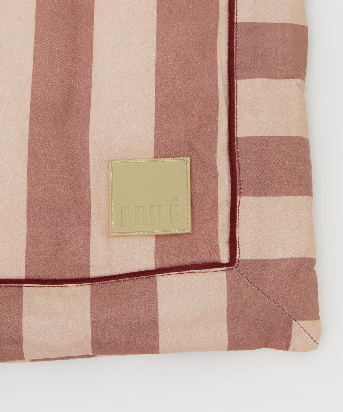 A close-up of the Philé - Striped Play Mat Pink by PHILÉ, made from eco-friendly OEKO-TEX cotton with wide and narrow dusty pink stripes and a beige PHILÉ label sewn onto the fabric.