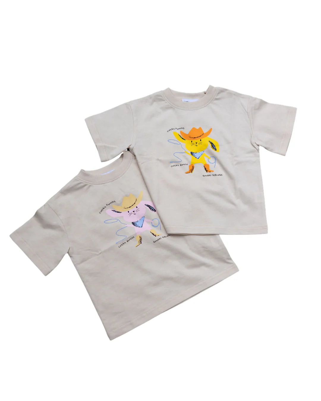 The Sunday Siblings - Catch'n Bunnies Tee Yellow by SUNDAY SIBLINGS is an oversized beige 100% cotton t-shirt featuring cartoon cats in hats dancing with musical notes and playful text—ideal for a fun Easter look.