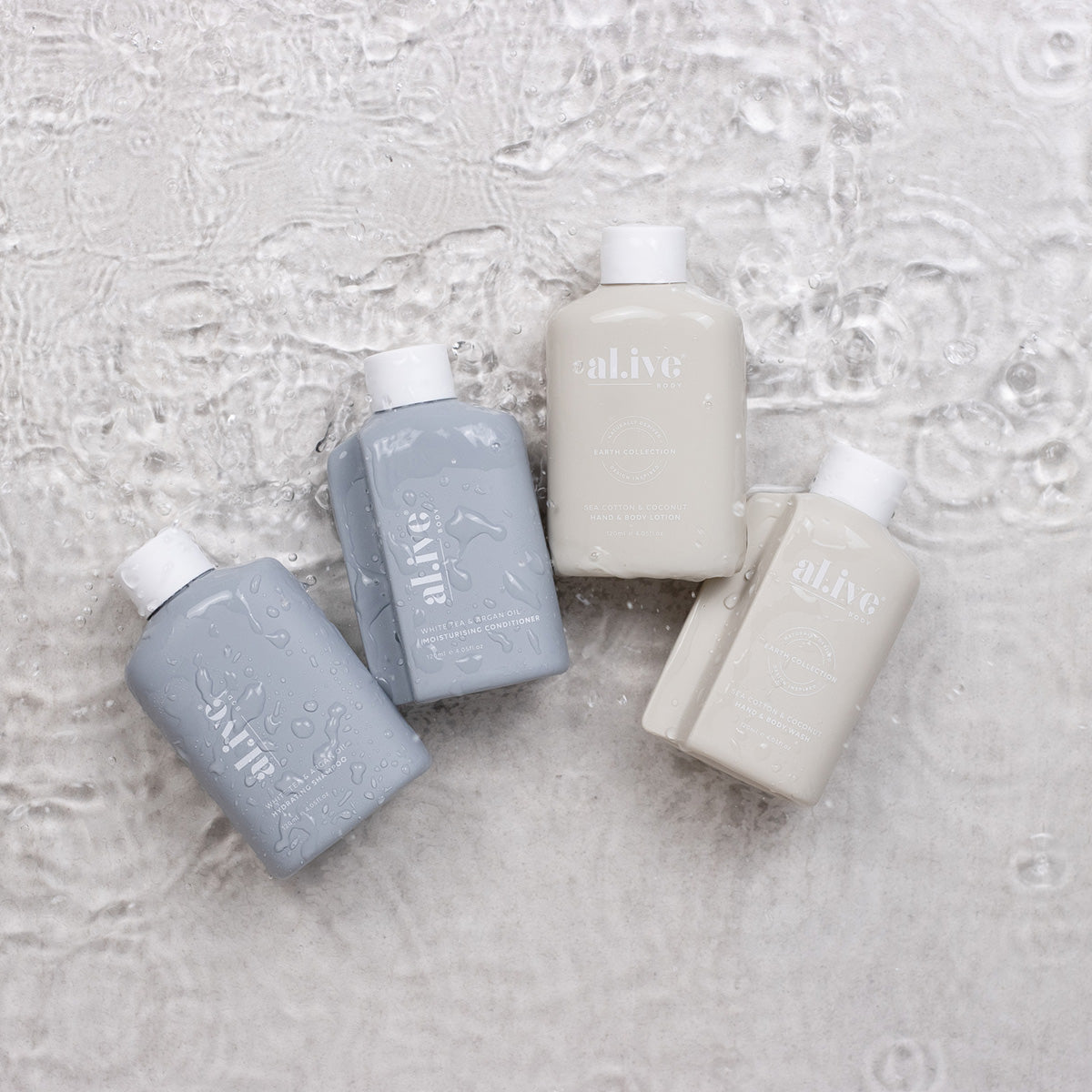 The al.ive body shampoo, conditioner, body lotion and body moisturiser laying down on the ground in some water.