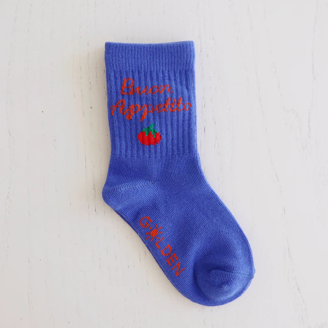 A single Buon Appetito Socks Pool Blue by GOLDEN CHILDREN, featuring red text and a small tomato design, with “GOLDEN” in red on the reinforced toe caps, is shown on a white wooden surface.