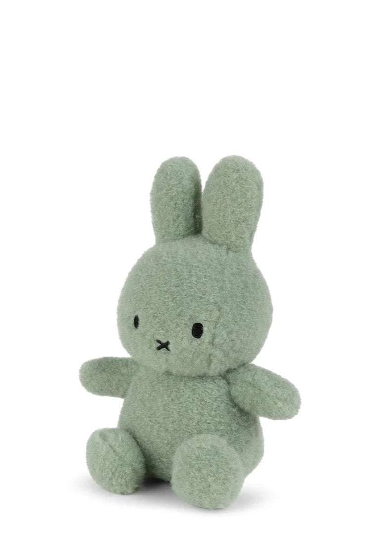 The 23cm Miffy ECO Cotton Candy Pistache from BON TON TOYS X MIFFY is a small, plush green bunny made from recycled polyester. It sits upright with minimalist black eyes and a tiny "X" mouth, reminiscent of Miffy. The plain white background highlights its adorable appearance.