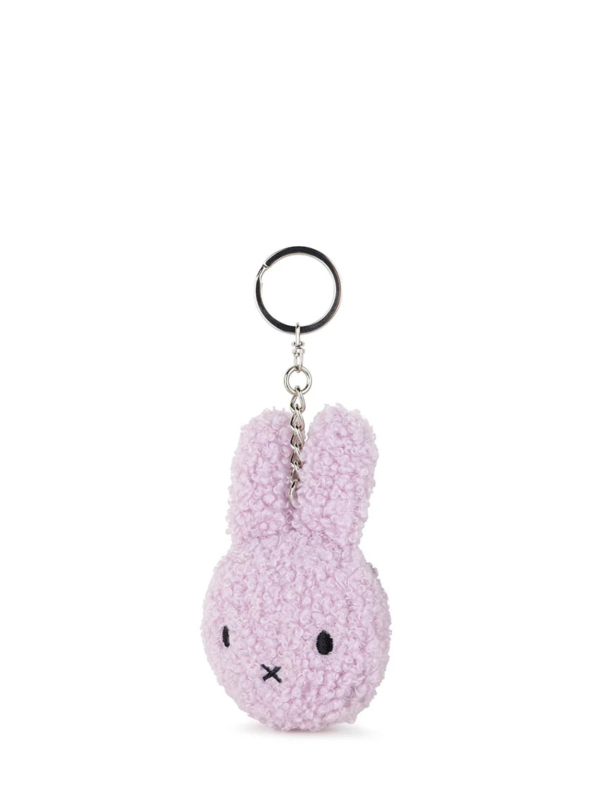 The Bon Ton Toys - Miffy Flat Keychain Tiny Teddy Lavender by BON TON TOYS X MIFFY is a light purple bunny head keychain with long ears, black embroidered features, made from recycled polyester and attached to a silver keyring.